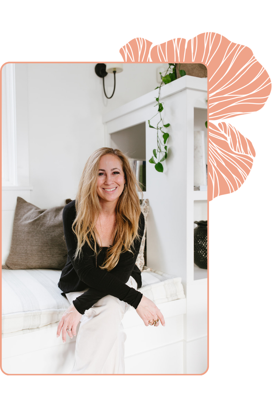 Tara standing in a modern Seattle kitchen with light gray cabinets, white farmhouse sink, quartz countertops, green plants, wood accents, and natural light from window