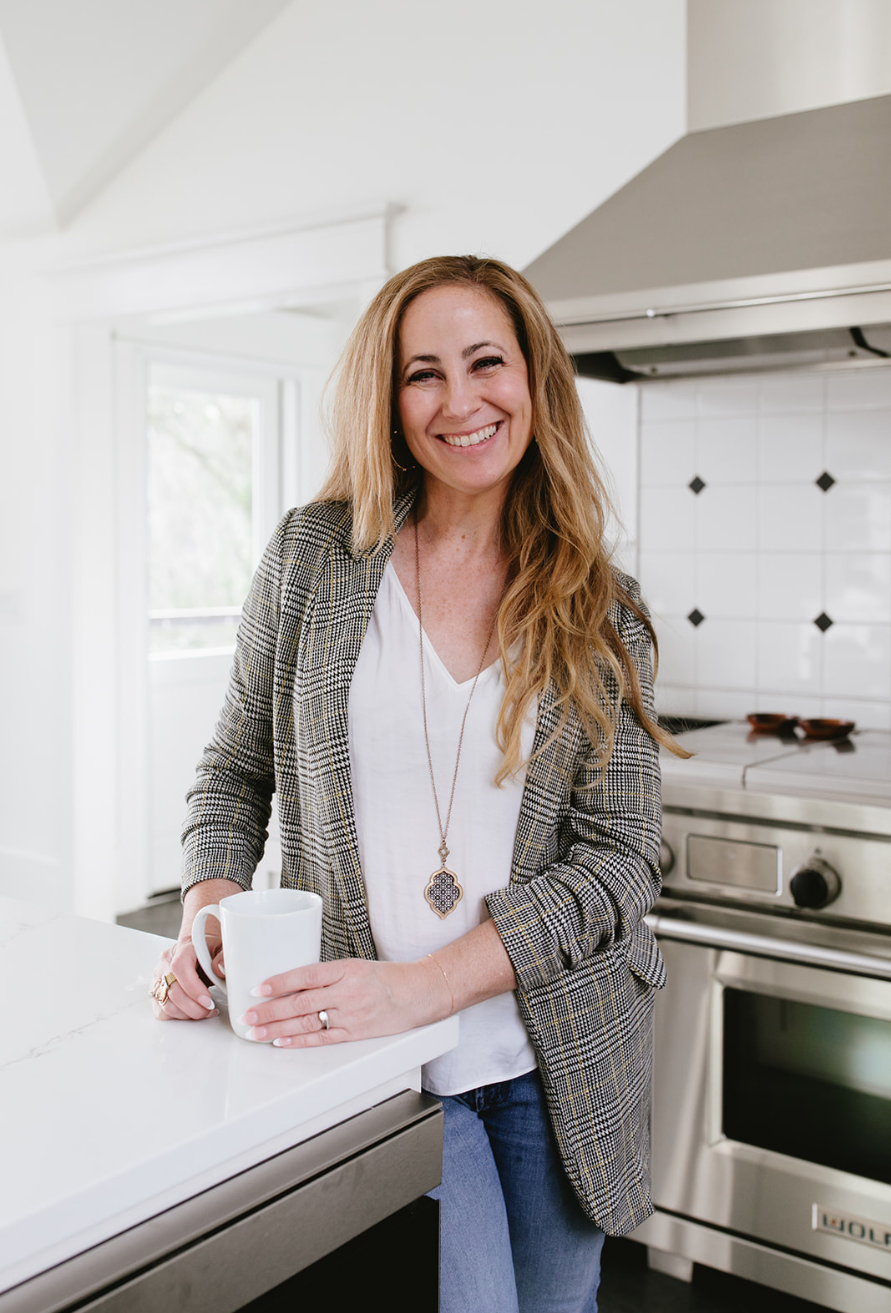 Tara Townsend Seattle real estate broker smiling in bright kitchen holding coffee, wearing plaid blazer and white top