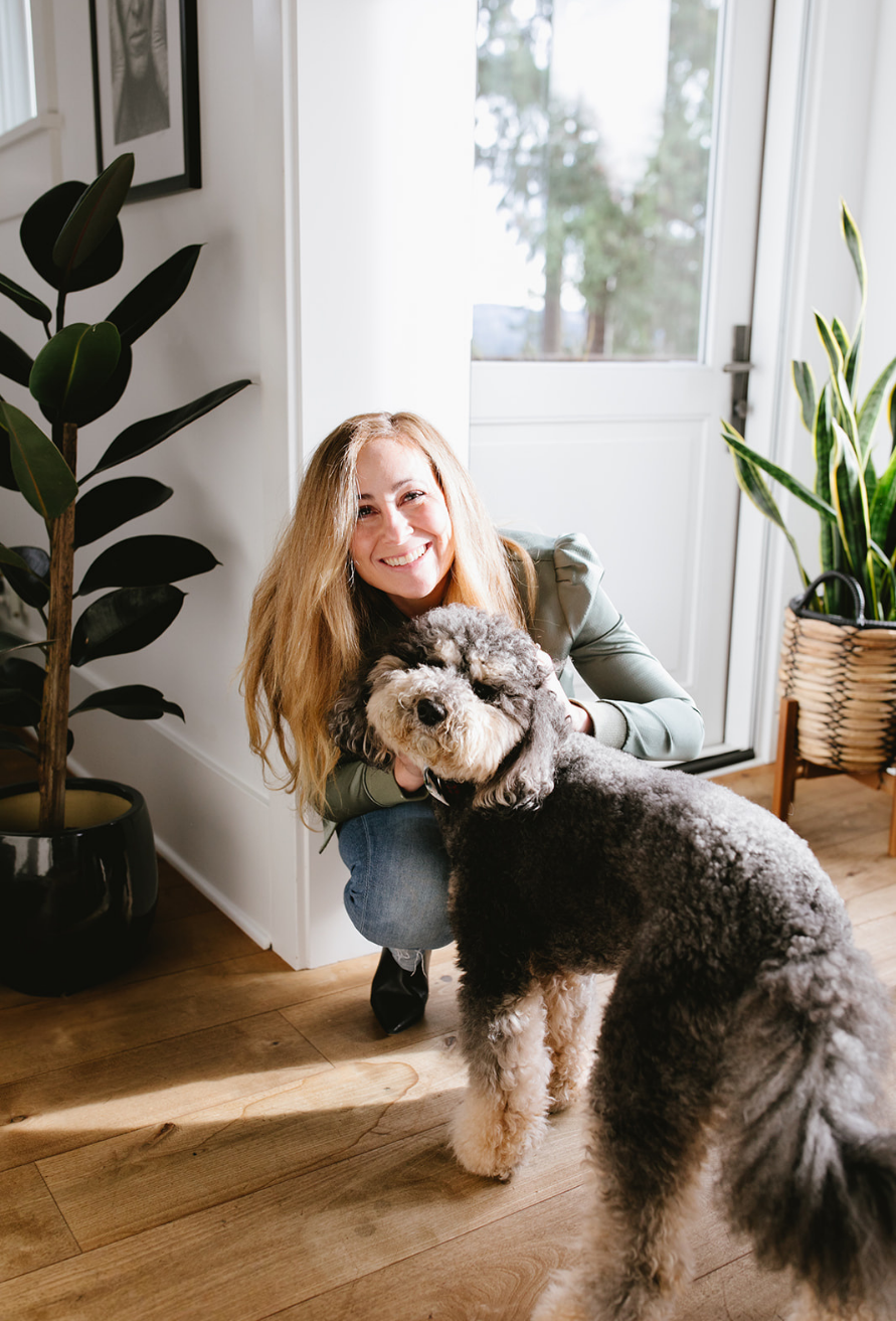 Tara, Seattle real estate agent sitting on white bench with beige cushions in bright modern interior, lifestyle portrait with natural light and neutral tones