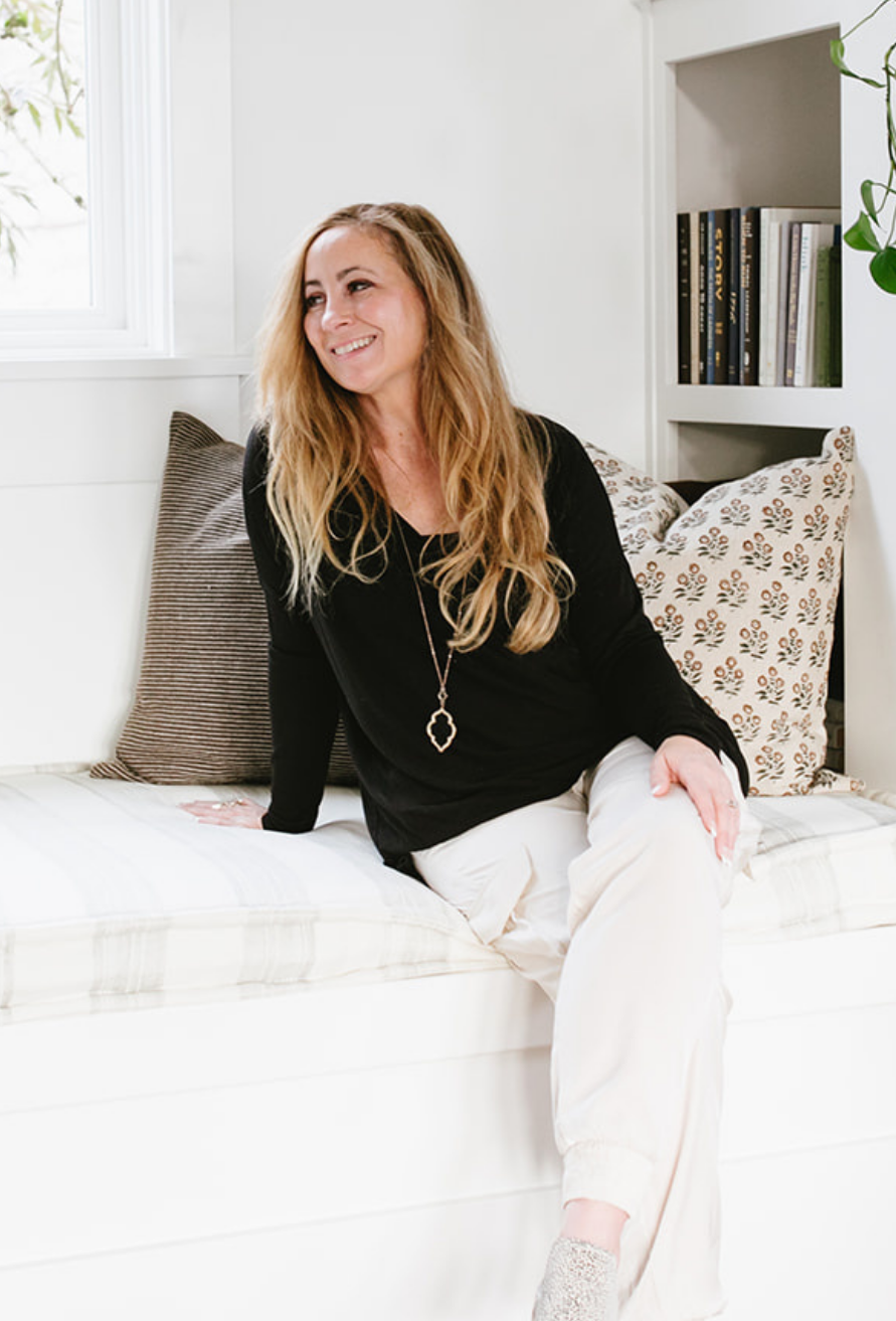 Tara Townsend real estate broker sitting on window seat in bright modern home with bookshelves, natural light, and neutral design