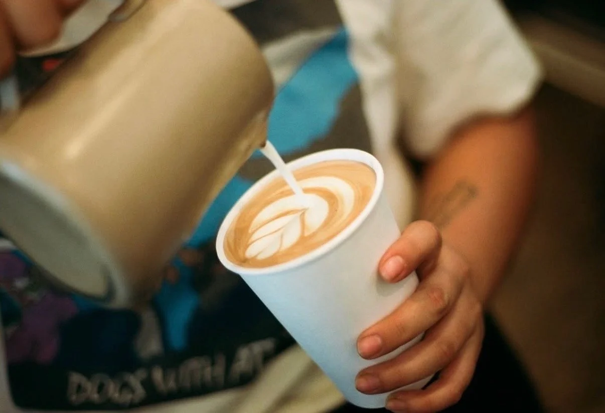 A person pouring milk into a cup of coffee to create latte art.