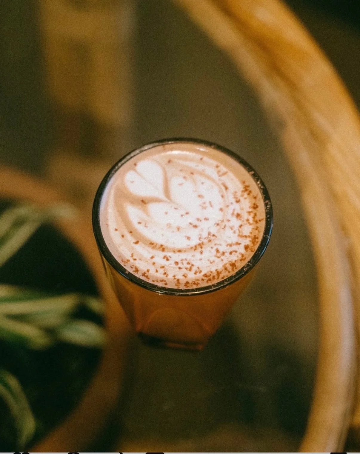 Top view of a tall glass of hot chocolate with whipped cream, chocolate shavings, and latte art on top, placed on a wooden table.