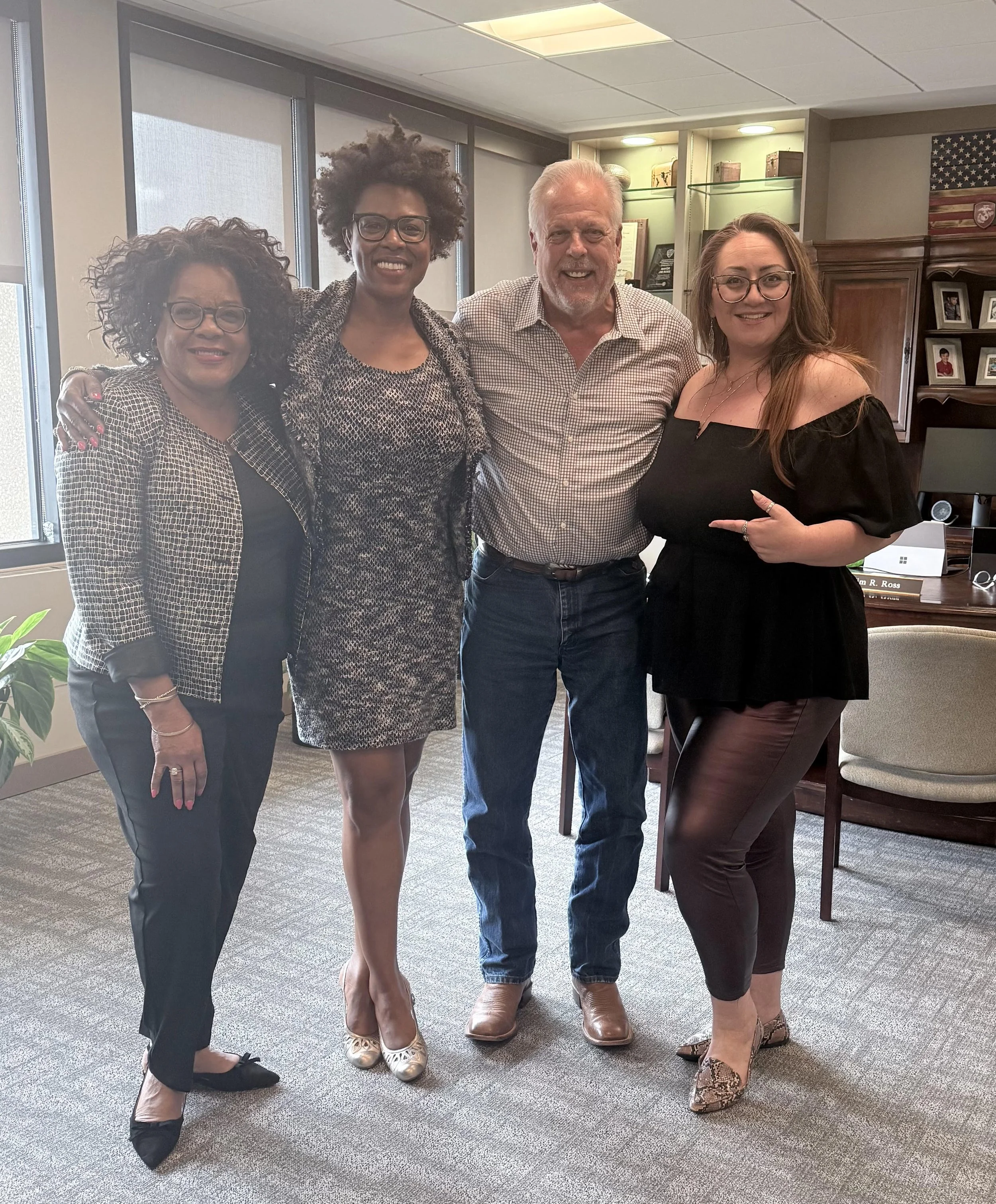 Four people standing together in an office, smiling for the camera.