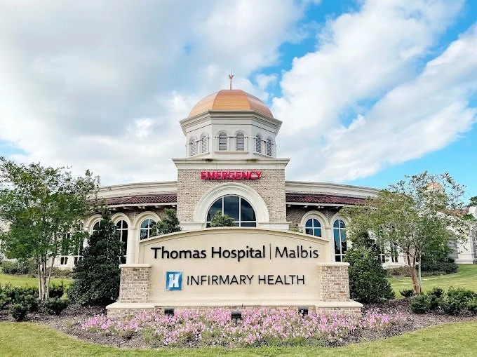 Front view of Thomas Hospital in Malbis with signs for emergency, Inpatient Health, and a domed roof under a partly cloudy sky.