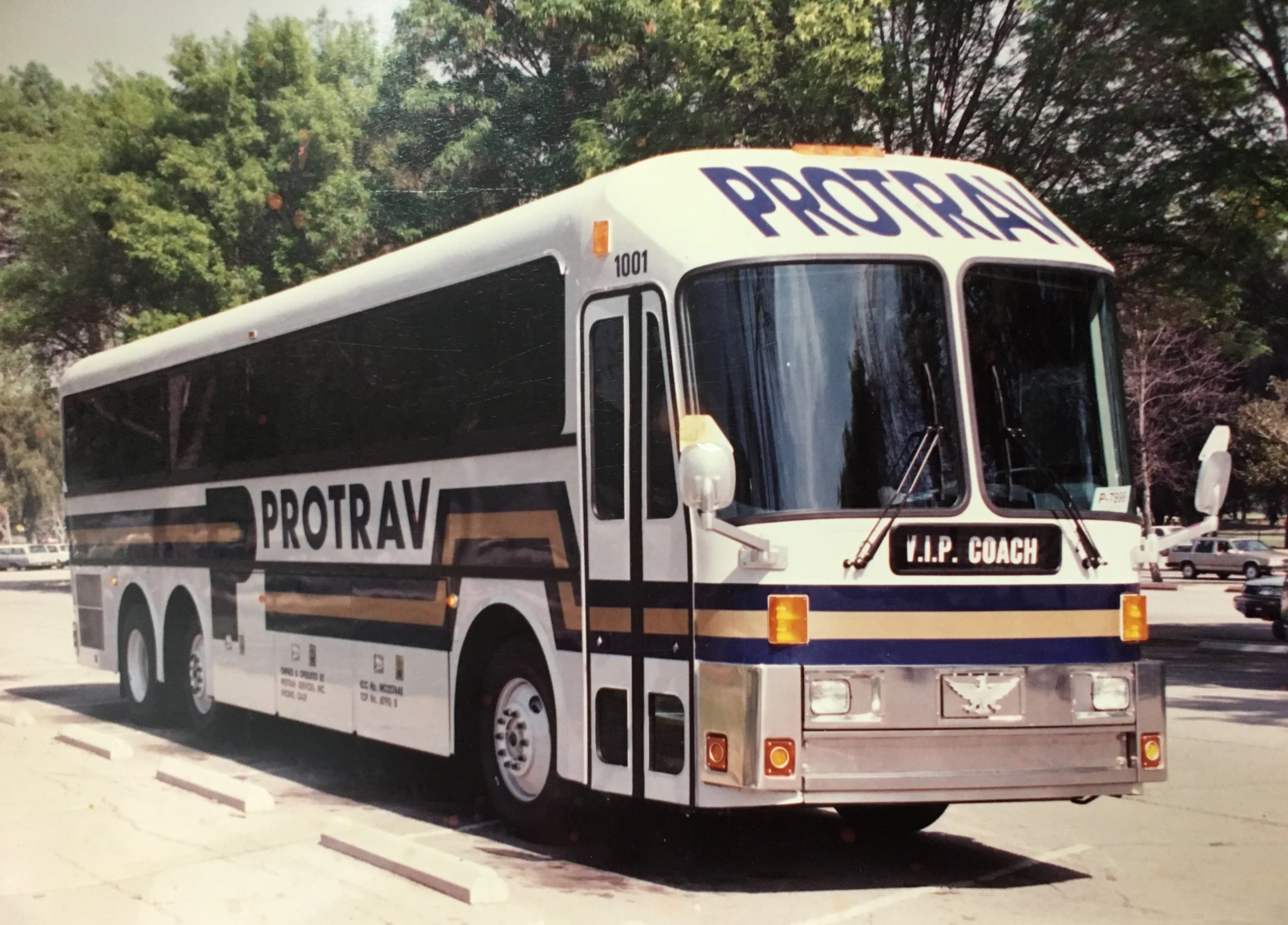 A vintage motor coach from the company PROTRAV' parked in a parking lot with trees in the background. The bus has the words 'V.I.P. COACH' on the front.