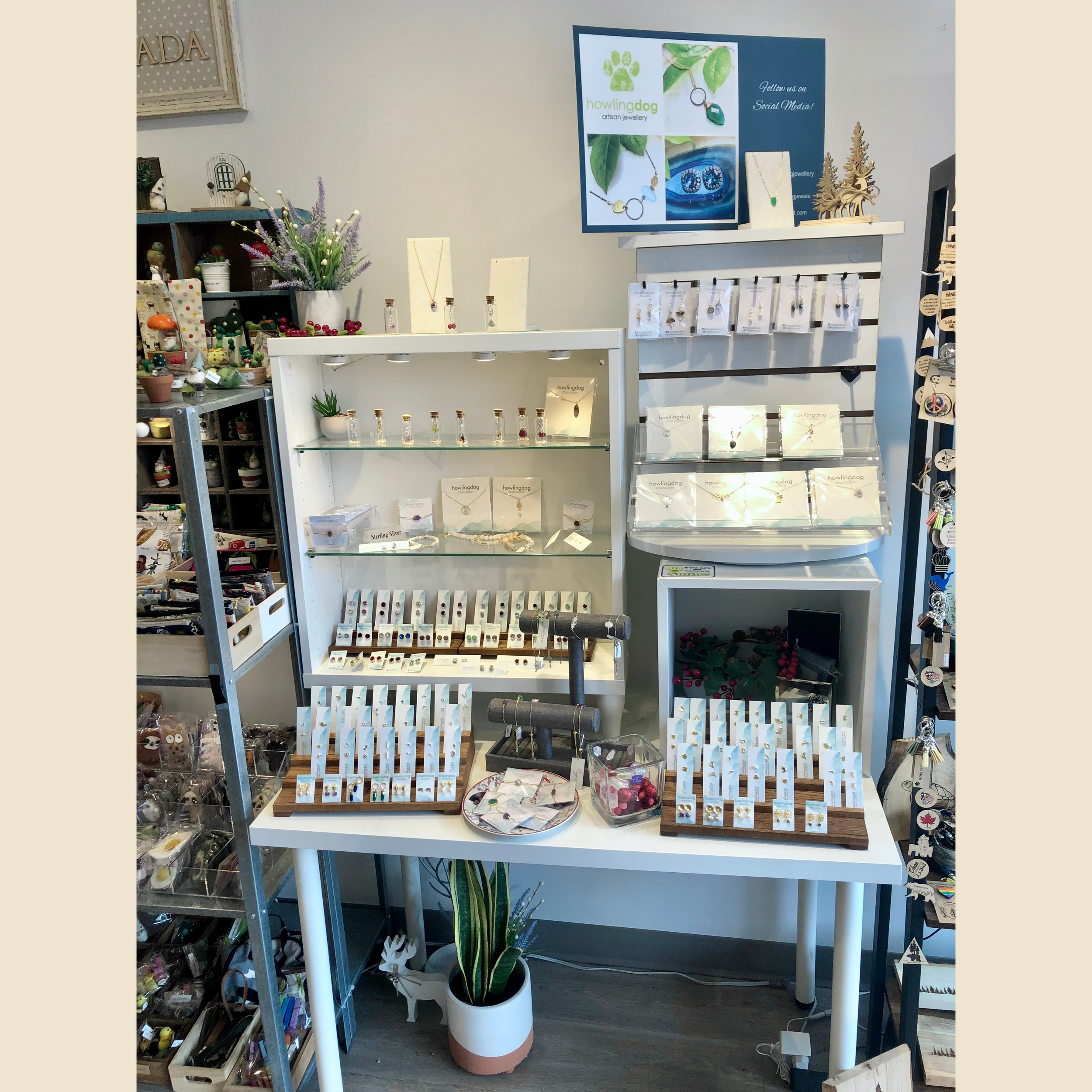 Display of jewelry on shelves and tables at a craft or gift shop, featuring necklaces, earrings, and other accessories, with signs and decorations around.