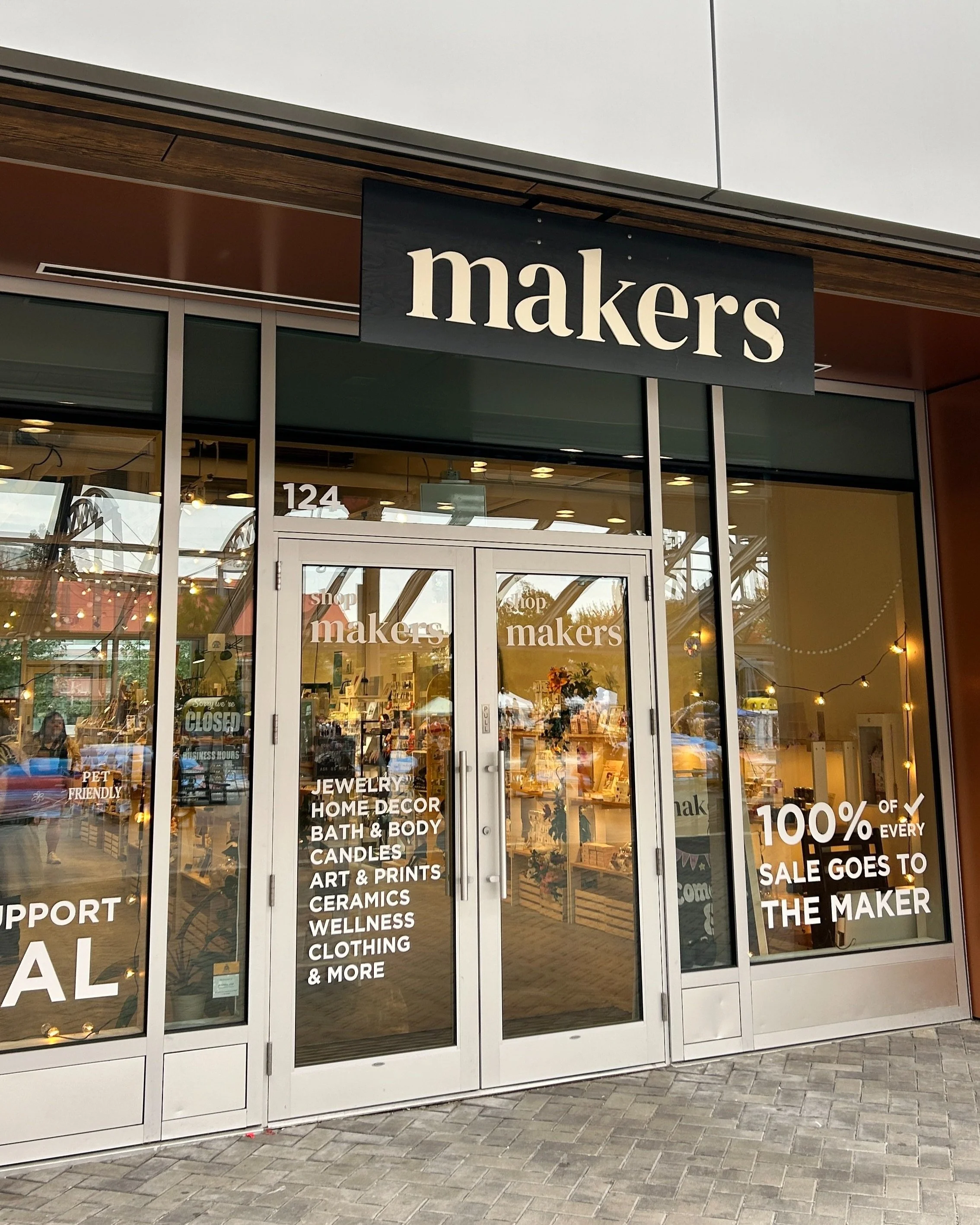 Storefront for 'Makers' with large black sign, glass doors with white text listing products, and interior displays visible through windows.