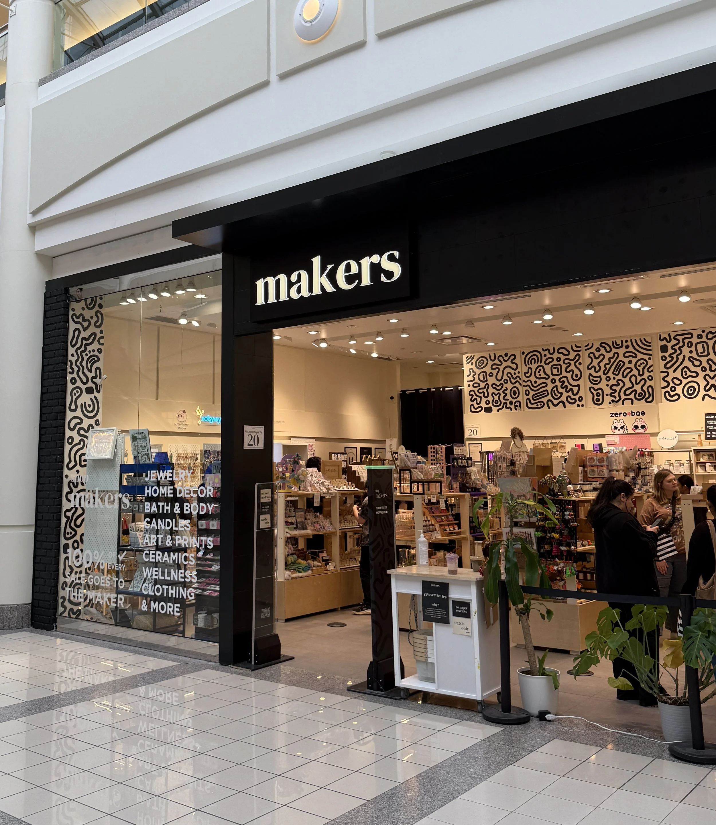 Storefront for 'makers' retail store inside a mall, with display shelves of various products and shoppers browsing inside.