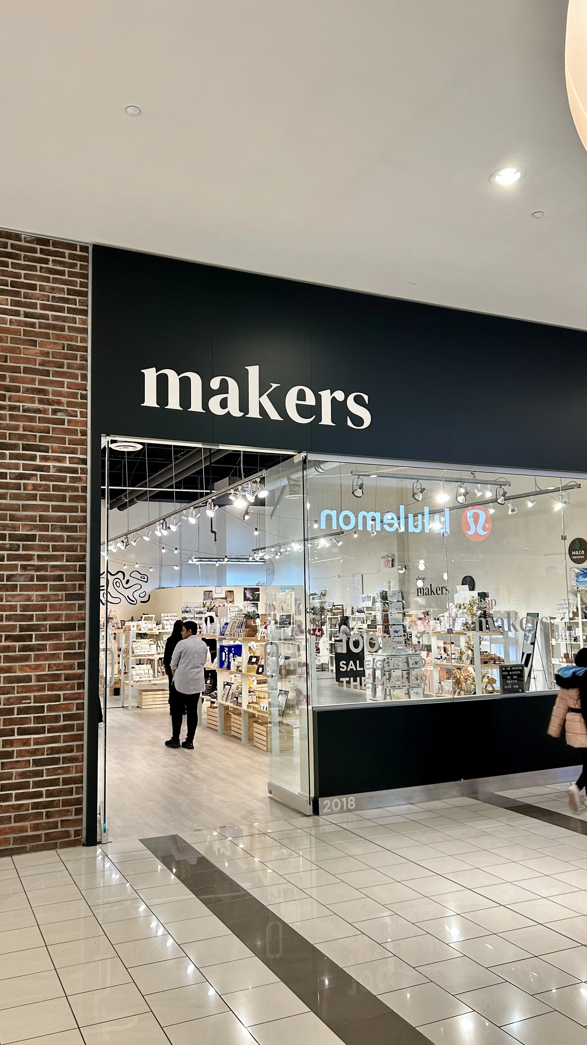 Entrance to a store called 'makers' inside a shopping mall, with visible interior shelves and customers inside.