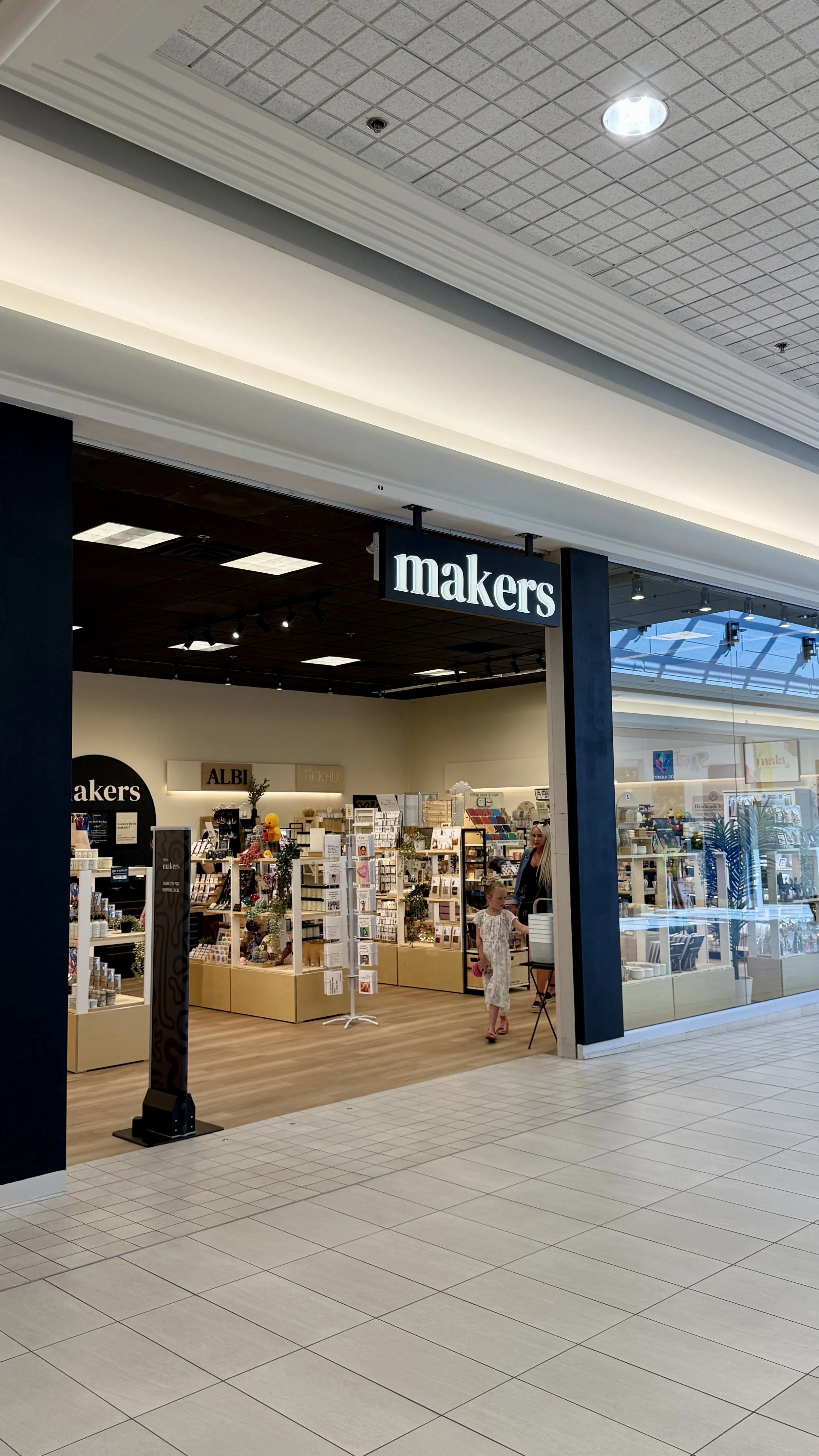 Storefront of 'Makers' boutique shop inside a shopping mall with a signboard, display tables, and two children walking in.