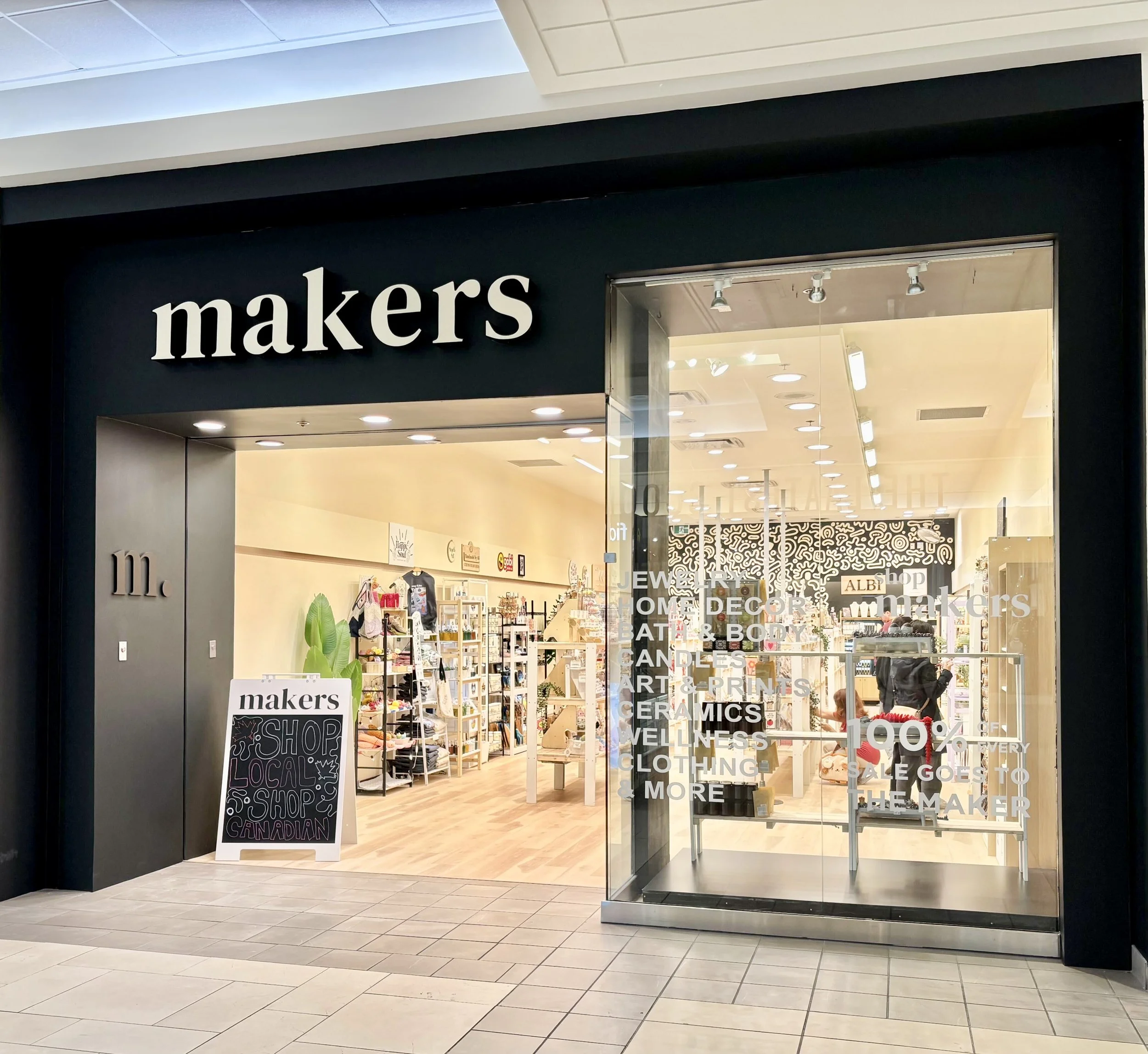 Storefront of 'Makers' retail shop with black exterior, large glass window, and sign board outside advertising local shop and Canadian products.