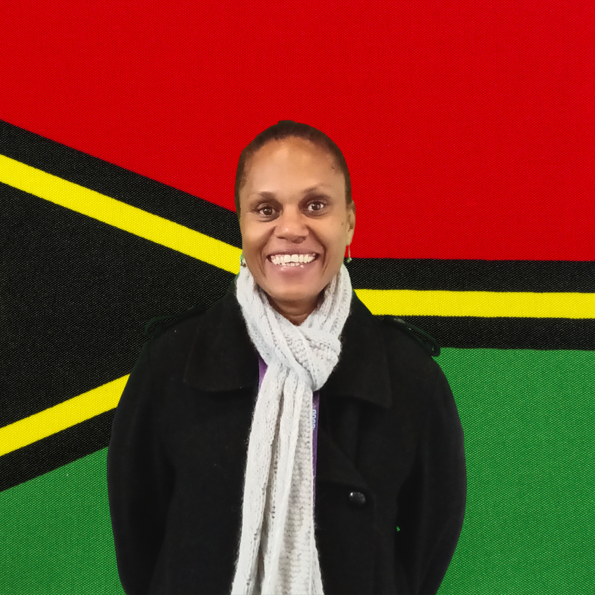 Esmie Jimmy founder of Green Forest Oils wearing a black coat and a white scarf, standing in front of the Vanuatu flag