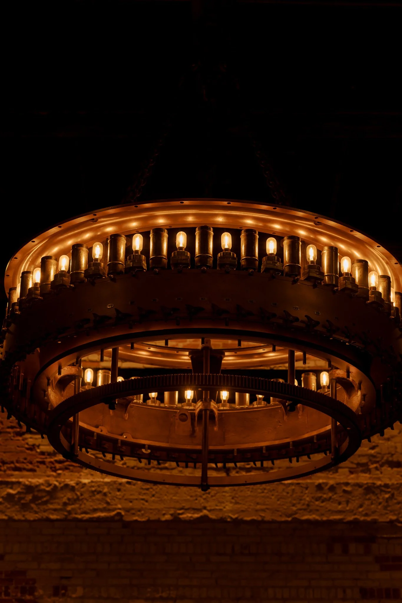 Close-up of a vintage chandelier with multiple glowing light bulbs, mounted on a brick wall.