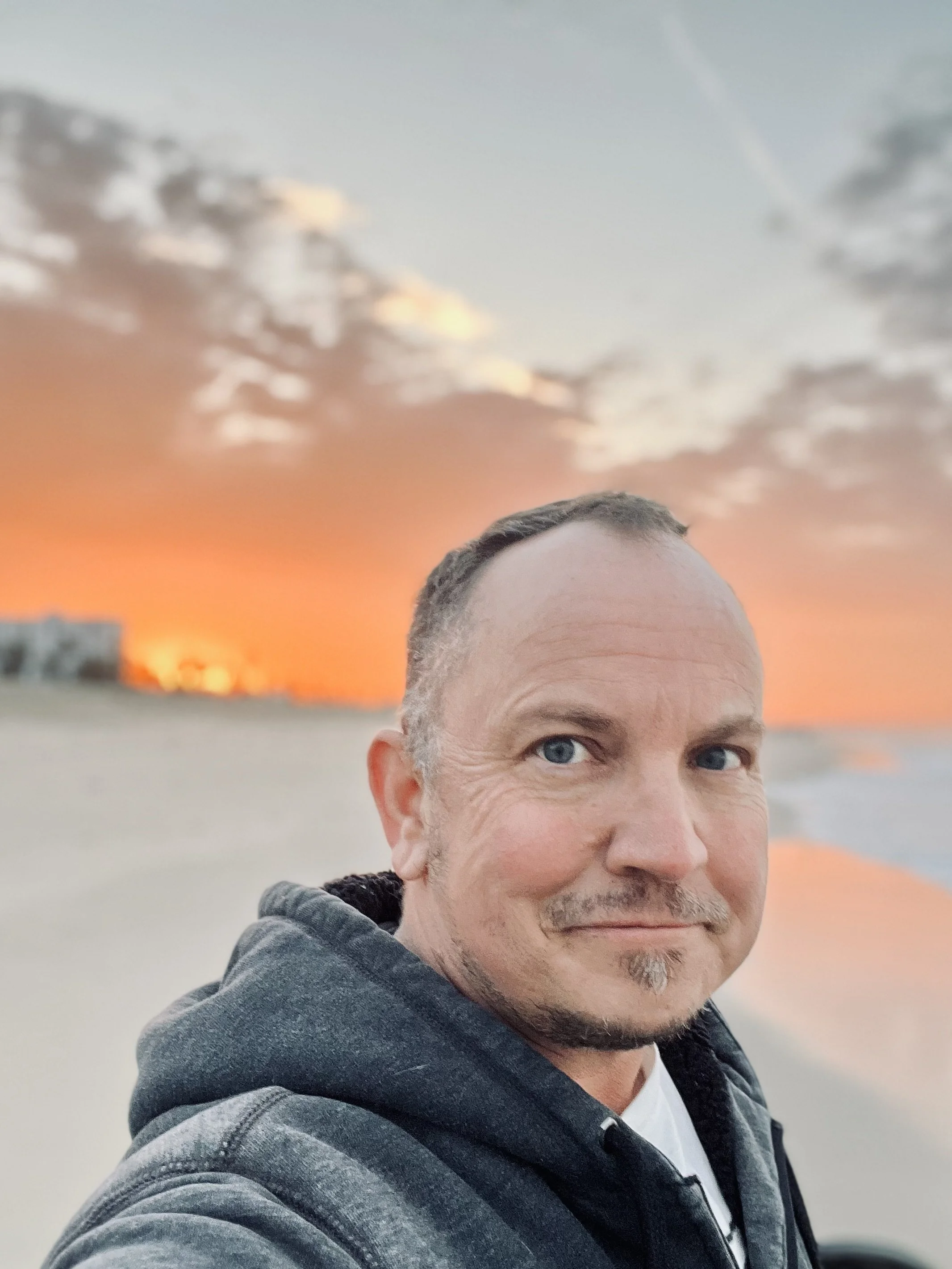 Nik Goodyear selfie at the beach against an orange sunset sky