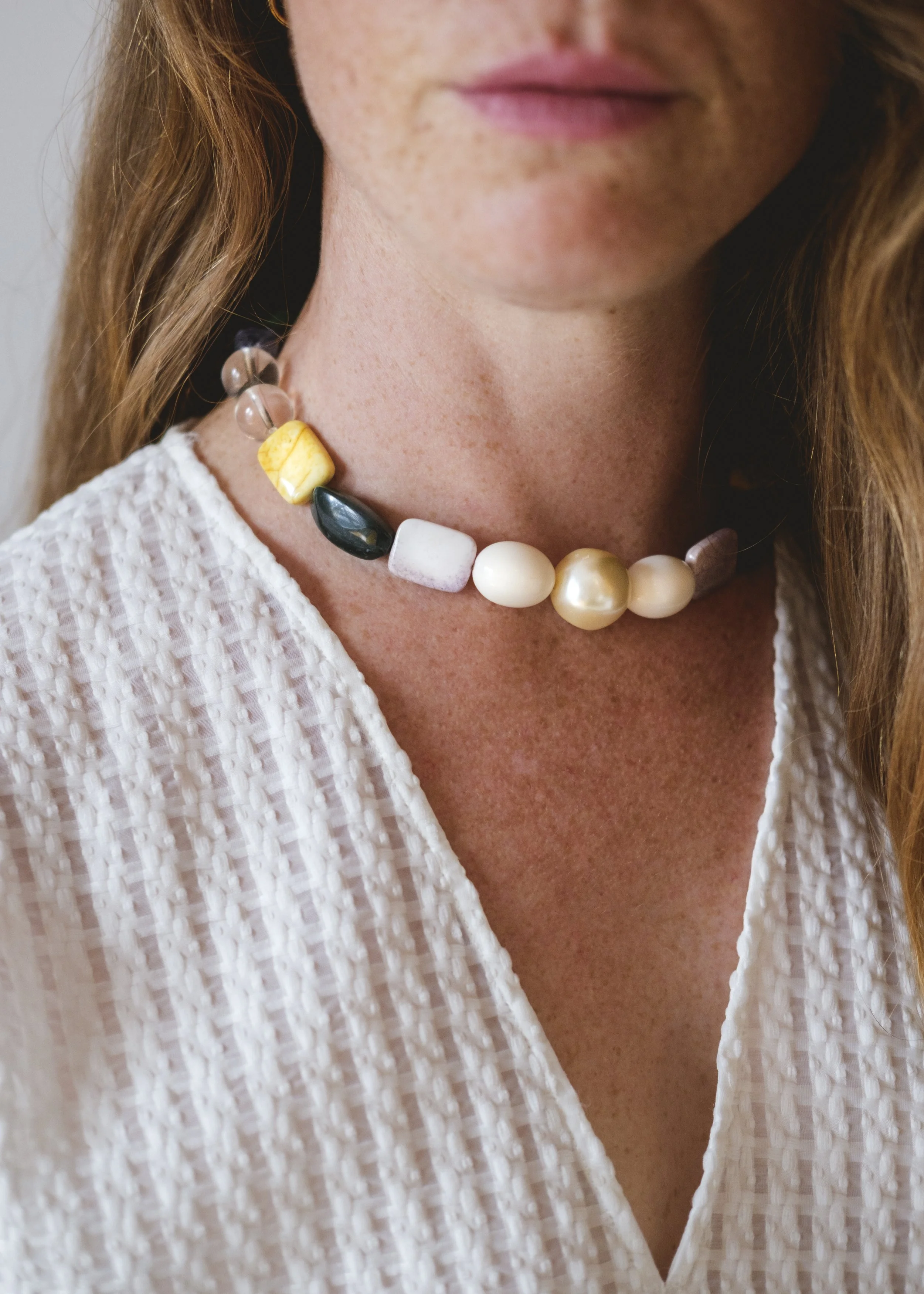 Un gros plan du cou d'une femme avec un collier de perles multicolores upcyclées élégant, portant une robe blanche en tissu texturé.