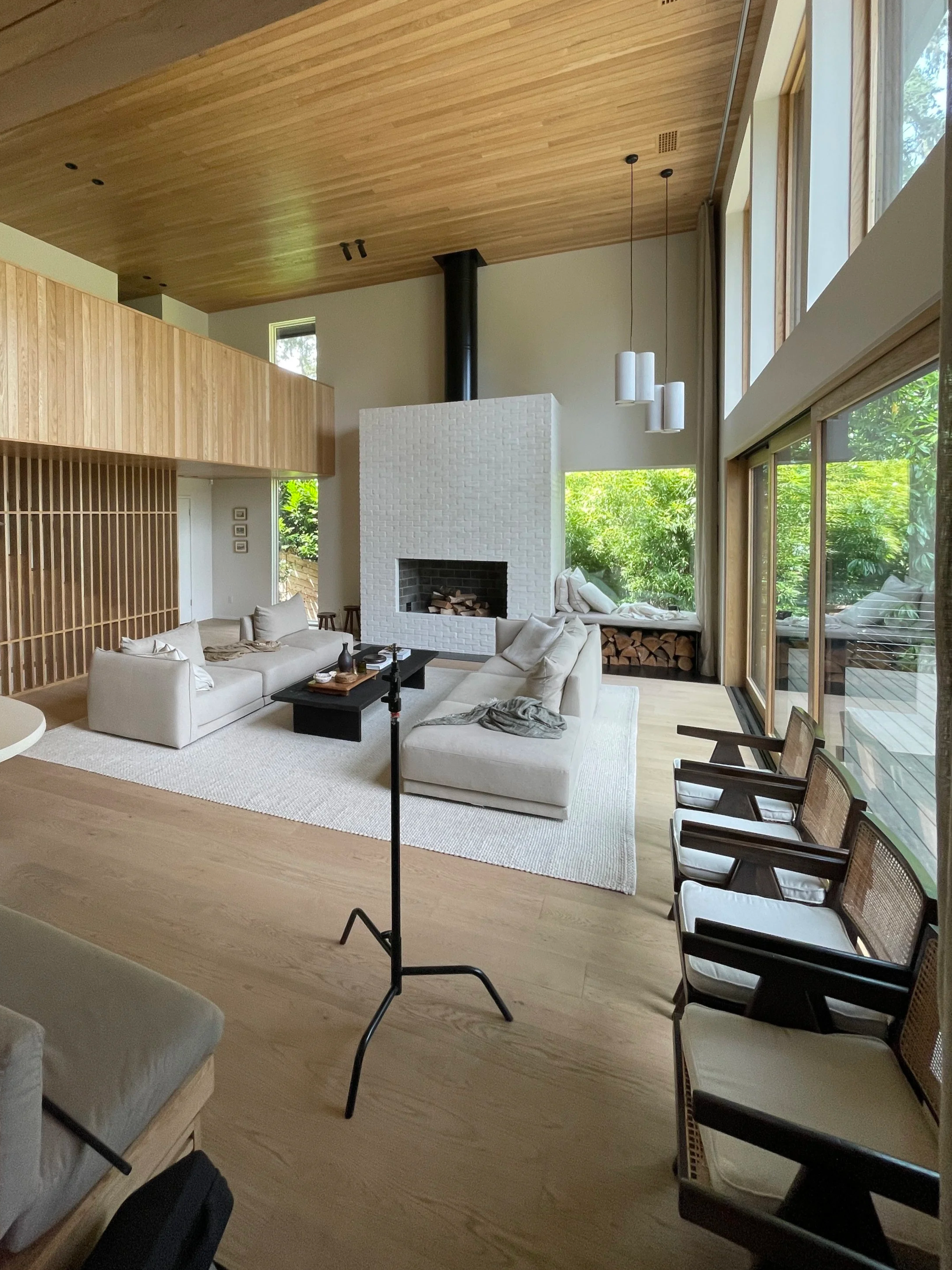 modern home with high ceilings, white couches and large windows, with a c-stand and other camera gear visible