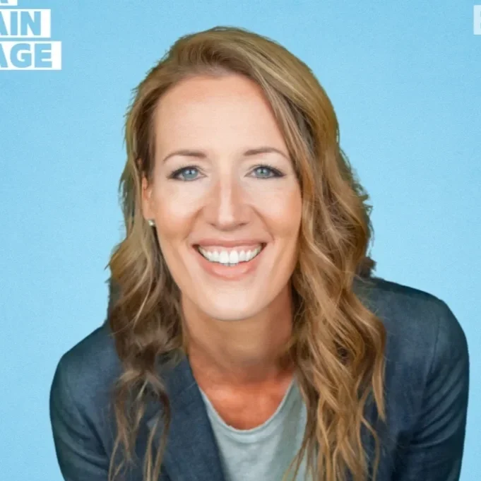 A woman with wavy, light brown hair and blue eyes, smiling, wearing a gray shirt and a blue denim jacket, against a light blue background with some partial text in the top left corner.