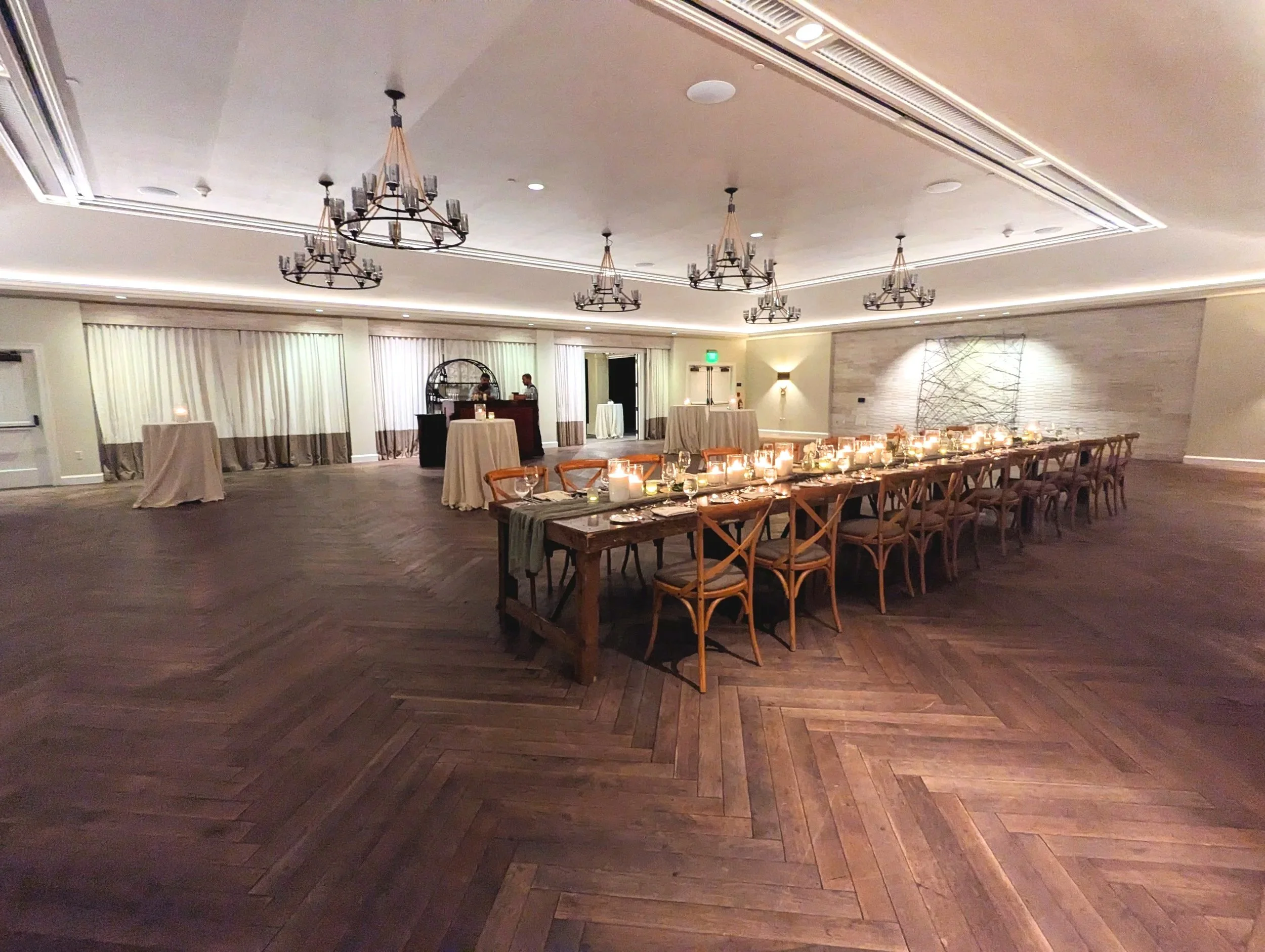 farm style banquet table decorated with lit candles, table runner, surrounded by wooden cross-back chairs