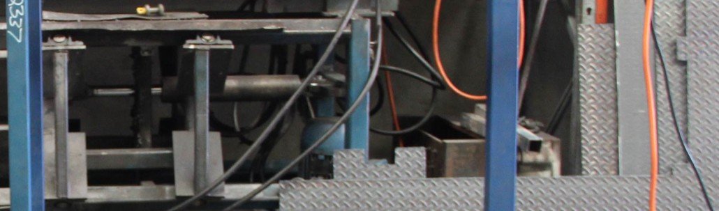 Close-up of industrial machinery with metal components, wires, and a textured metal step in the foreground.