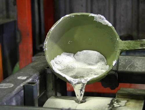 Green metal ladle pouring melted wax into an old sawhorse in a workshop.
