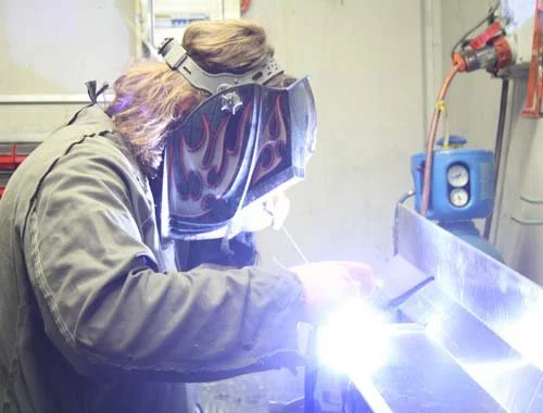 Person welding in a workshop with safety gear and equipment.