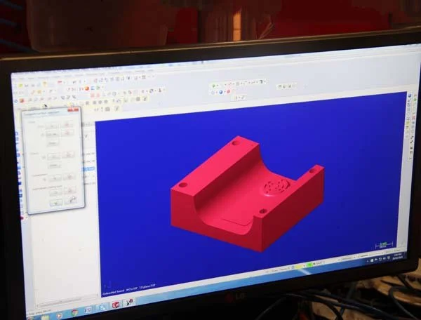 Computer monitor displaying a 3D CAD model of a pink mechanical part on a blue background.