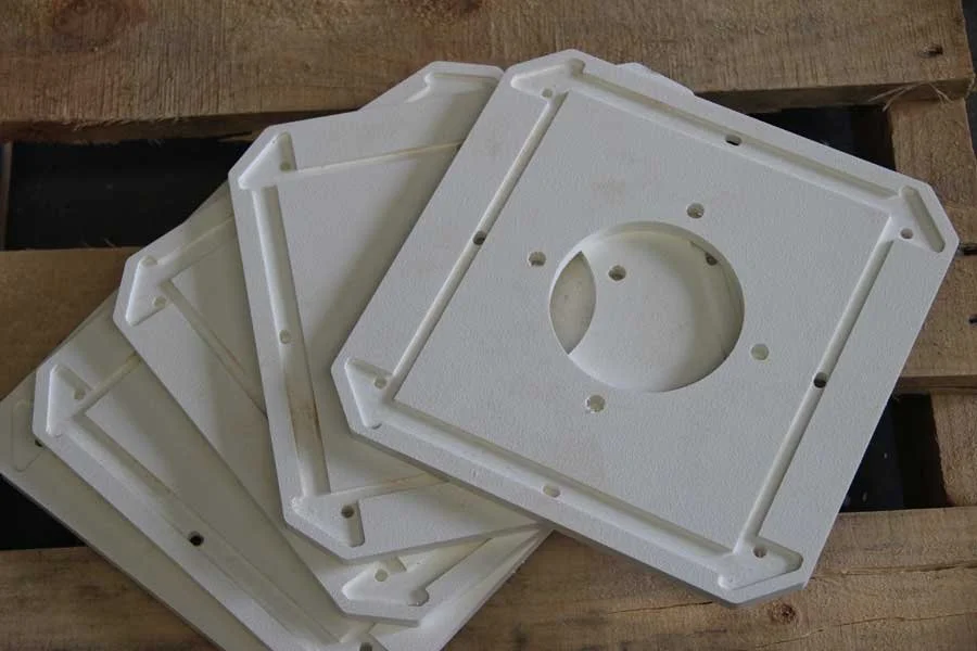 A stack of white rectangular plastic mounting plates with a circular cutout and multiple screw holes, placed on a wooden surface.