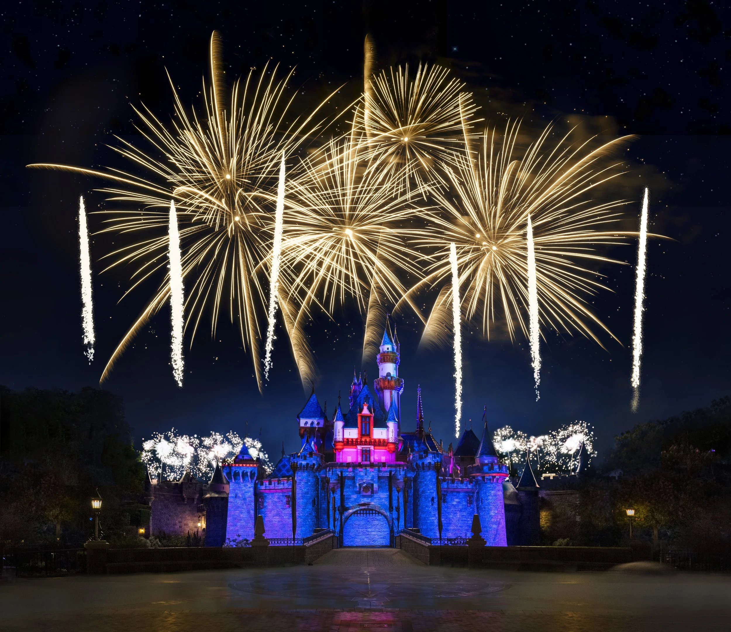 Fireworks display over a colorful castle at night.