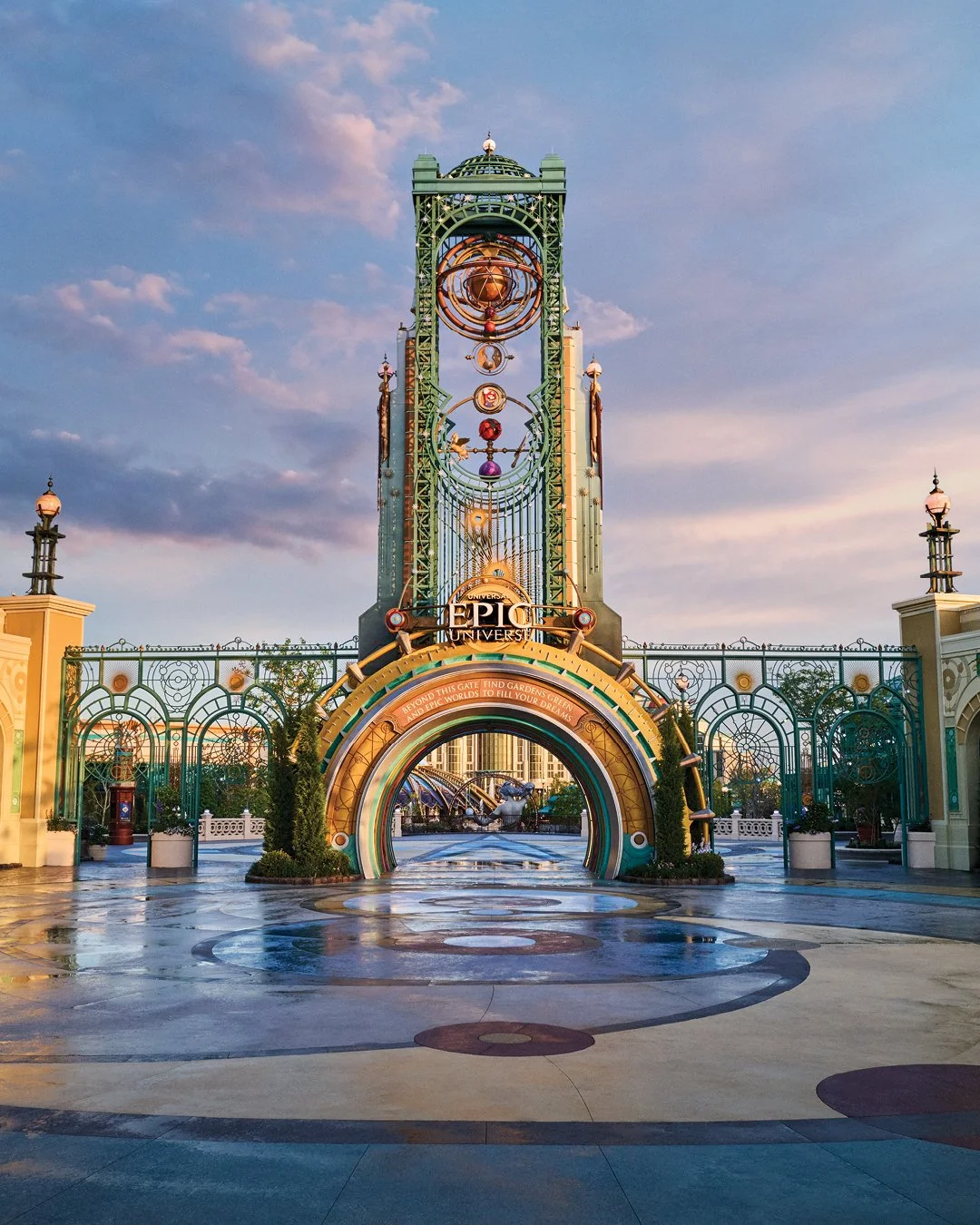Entrance gate to Disney's Epic Universe theme park with ornate metal arch and clock tower, under a partly cloudy sky.