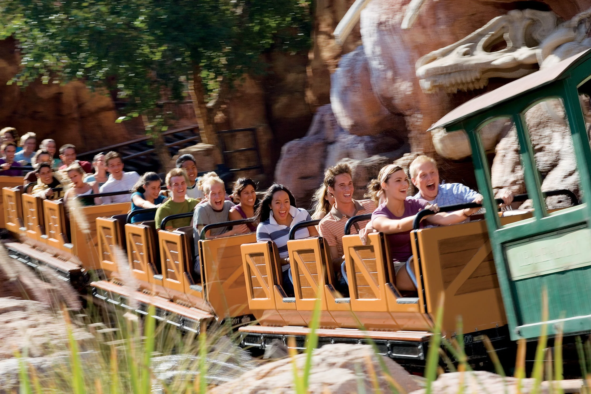 A group of people on a roller coaster ride at an amusement park, with some people smiling and laughing as they go around a bend.