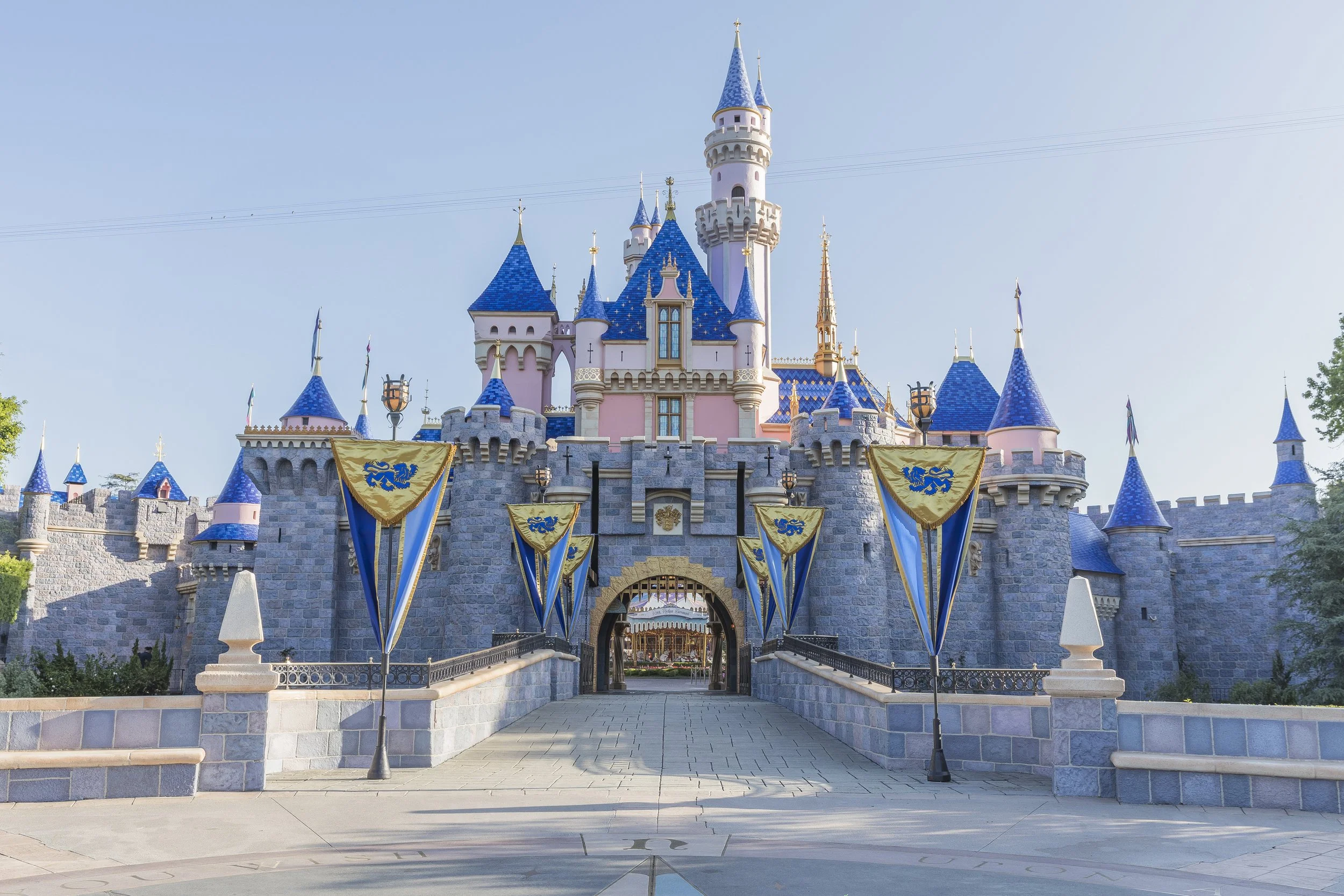 A pink and blue castle with multiple turrets and flags, resembling a fairy tale castle, at a theme park.