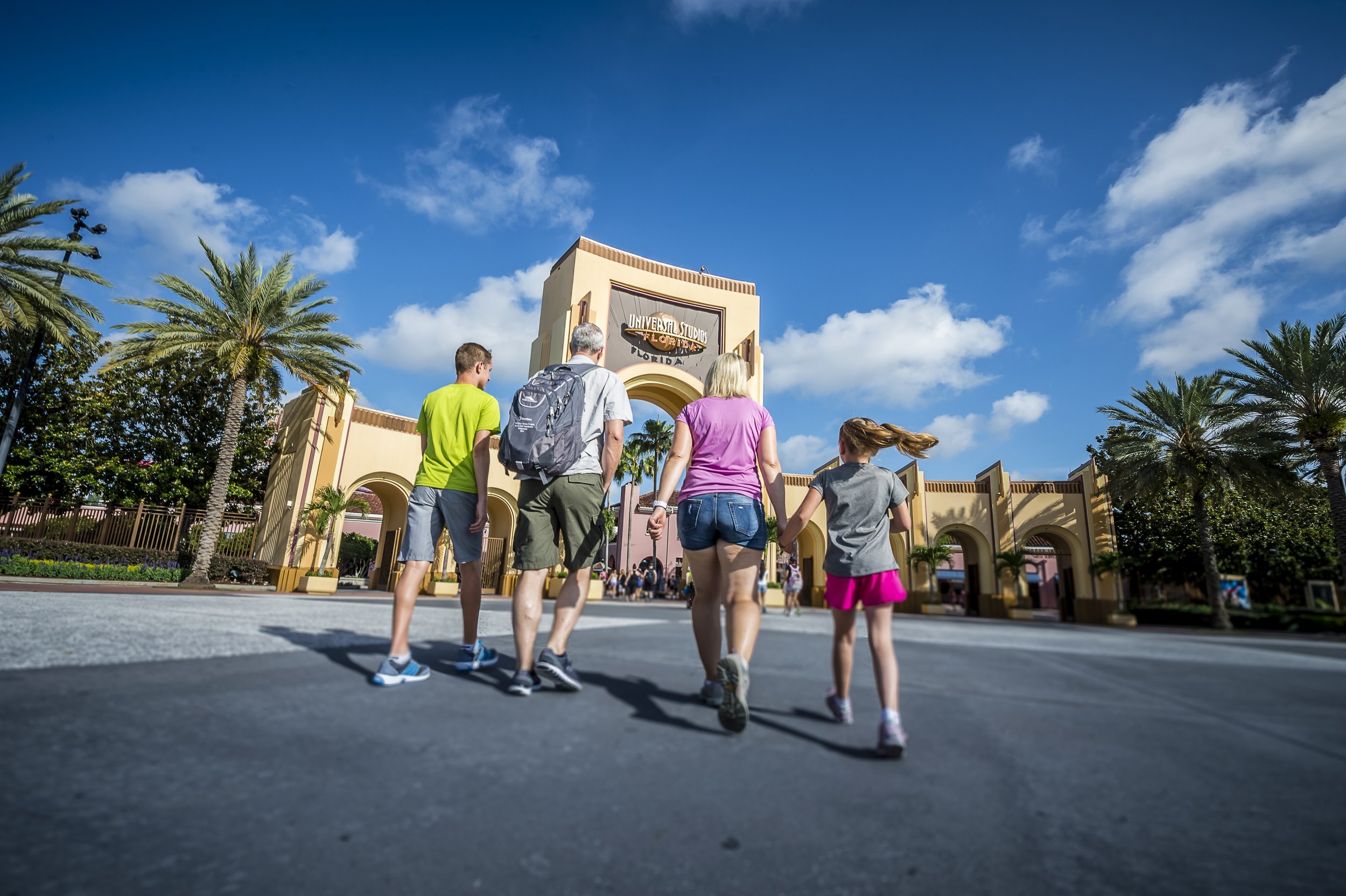 Family walking toward the entrance of Universal Studios Florida theme park on a sunny day with blue skies and palm trees.