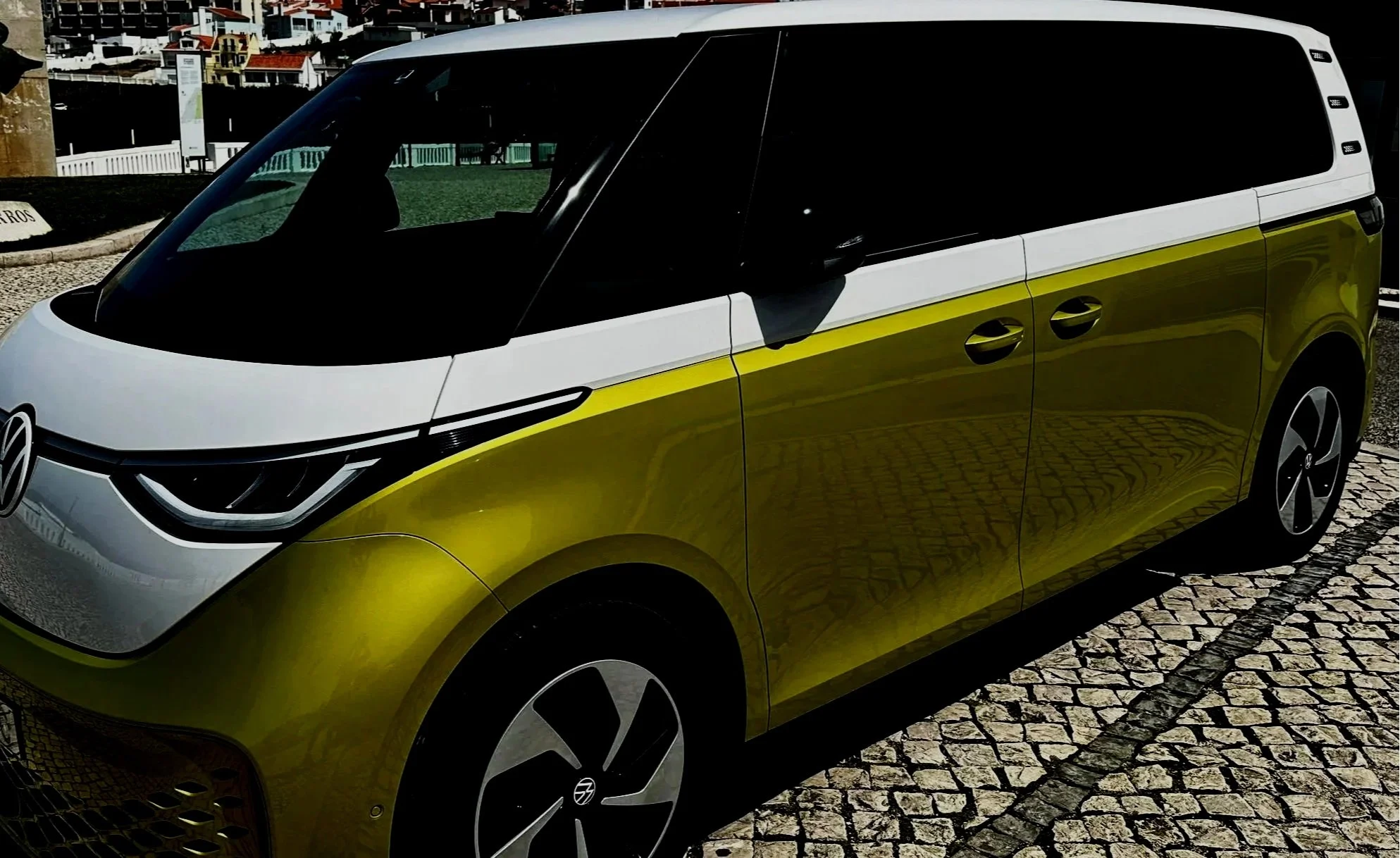 A yellow and white Volkswagen ID Buzz electric minivan parked on a cobblestone street.