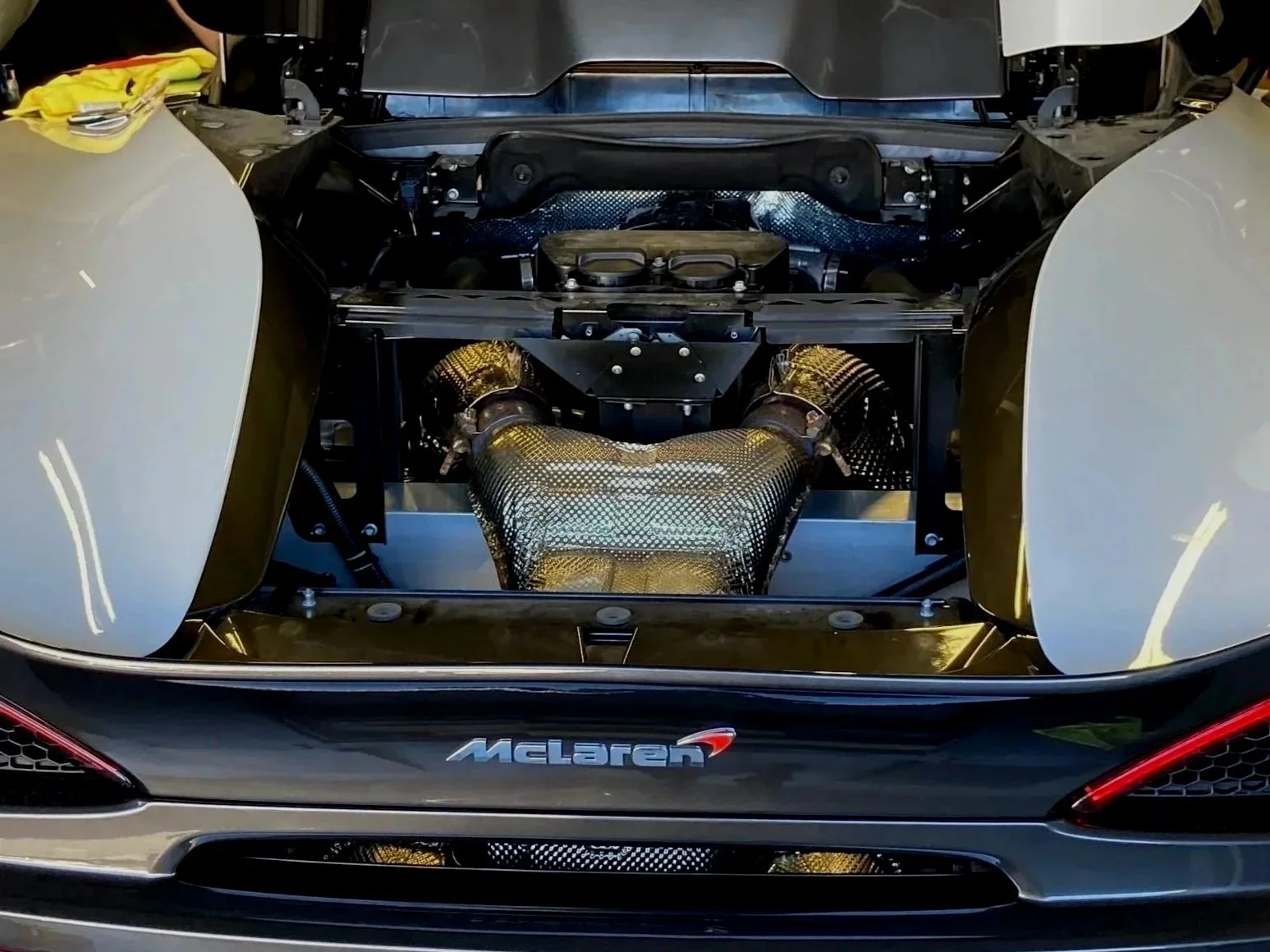 The rear of a McLaren 570s  with the engine cover removed, showing the engine and exhaust components.