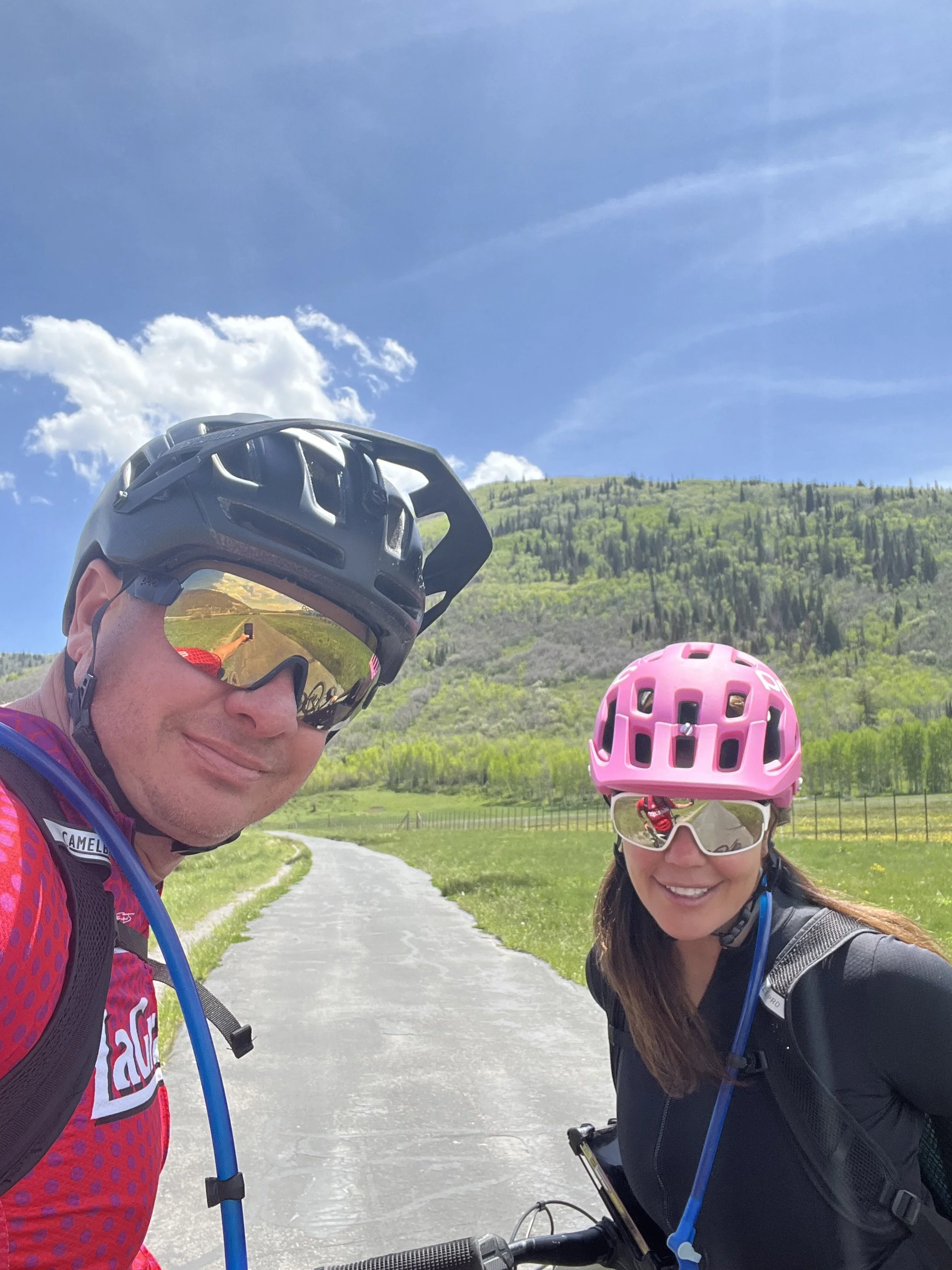 Brett and Karen Sutherlin take a selfie on a beautiful, green biking trail in Park City, Utah
