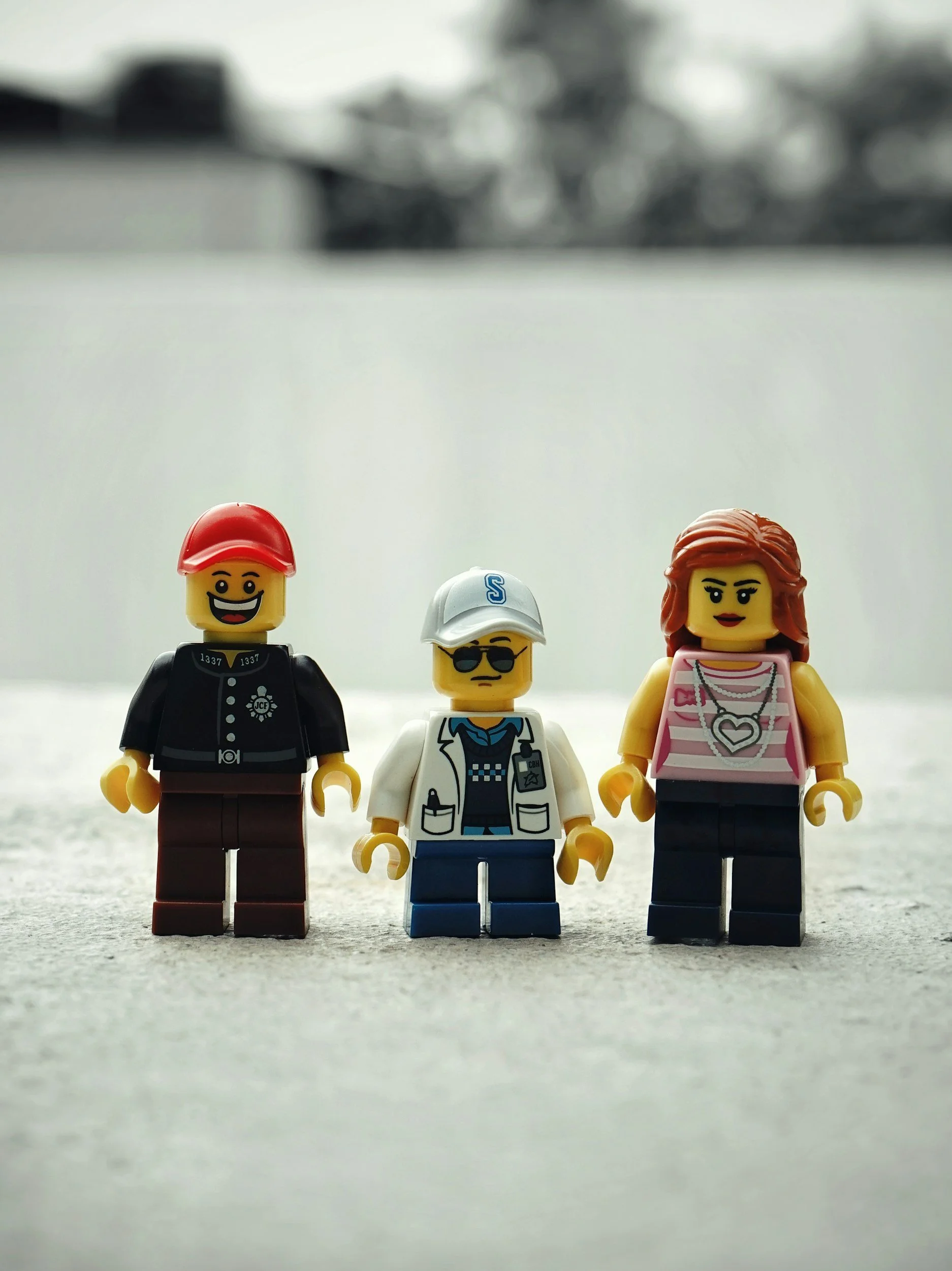 Three LEGO minifigures standing on a concrete surface outdoors.