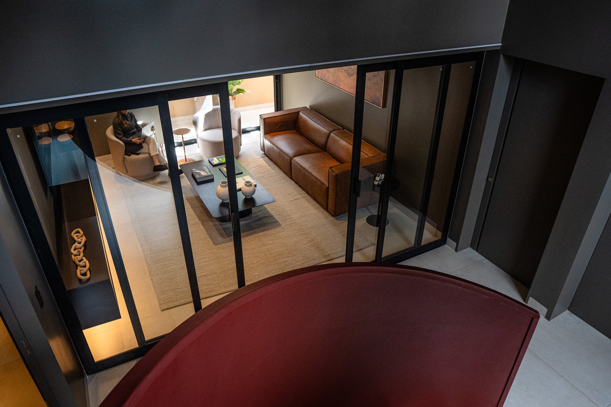 Sala de estar com sofá de couro marrom, mesa de centro com decorações e poltronas na varanda, vista de cima.