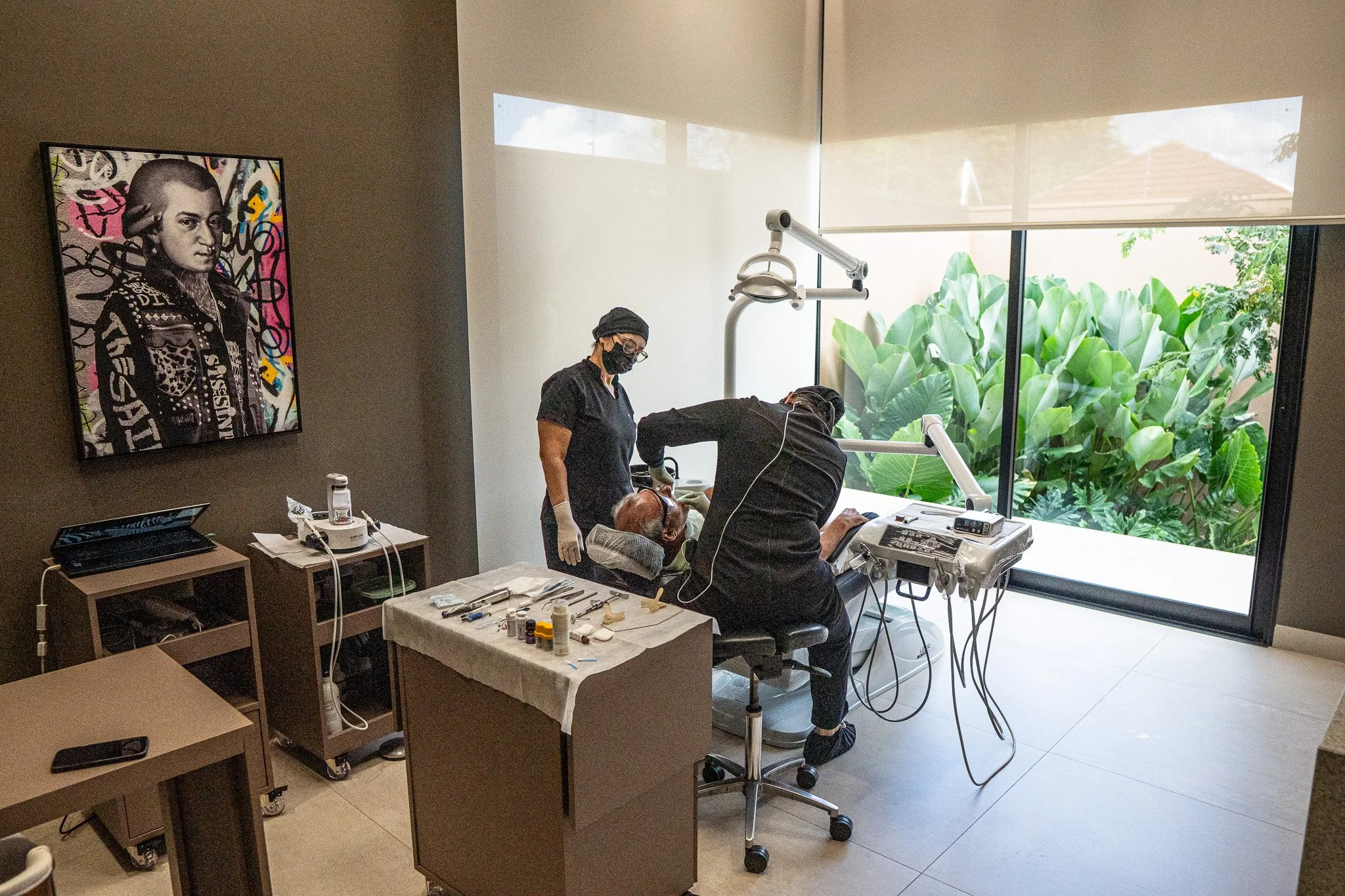 Dentista atendendo paciente em clínica moderna com grande janela e vegetação ao fundo.