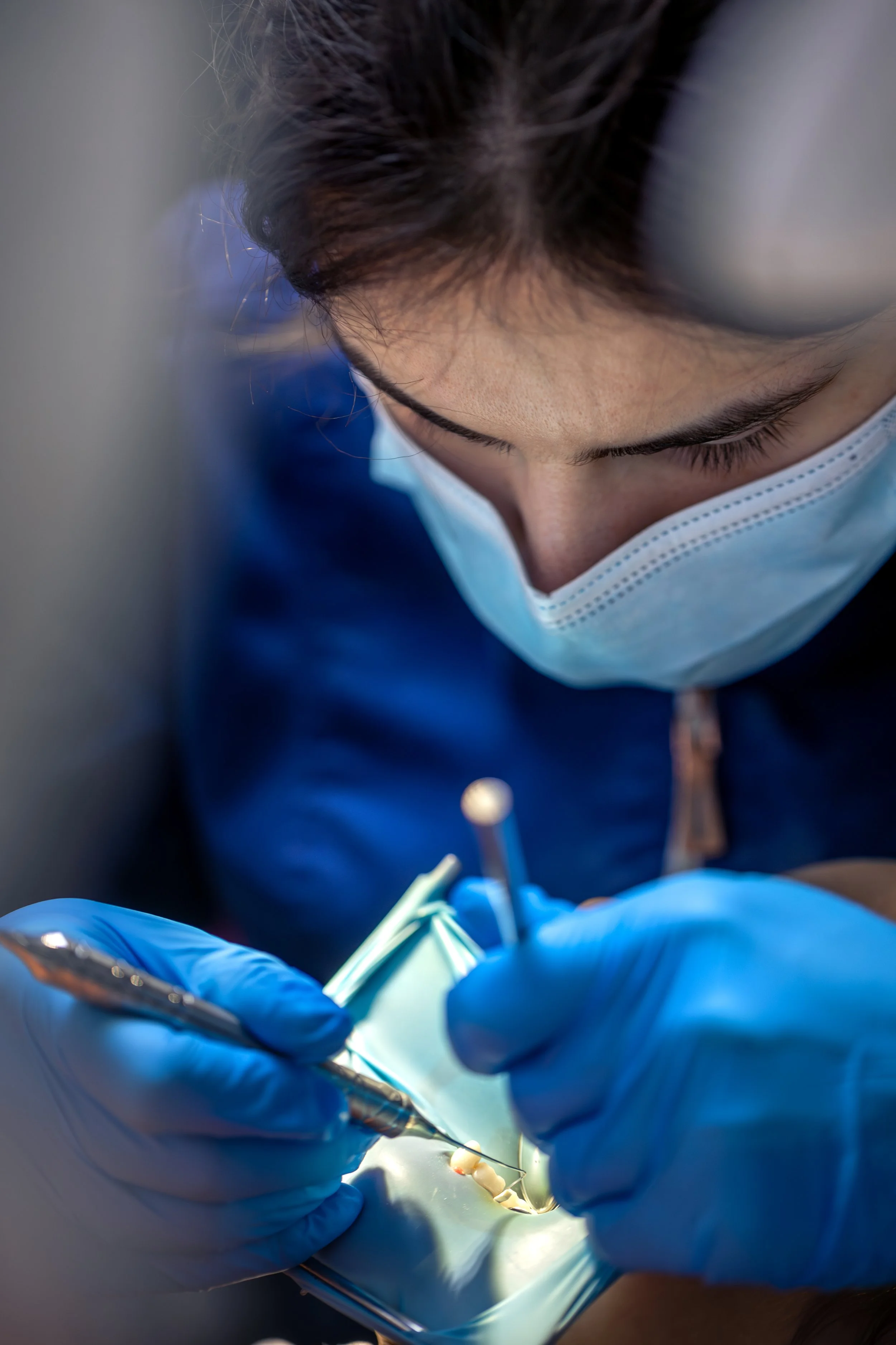 Dentista realizando procedimento odontológico com máscara e luvas, focada na boca do paciente.