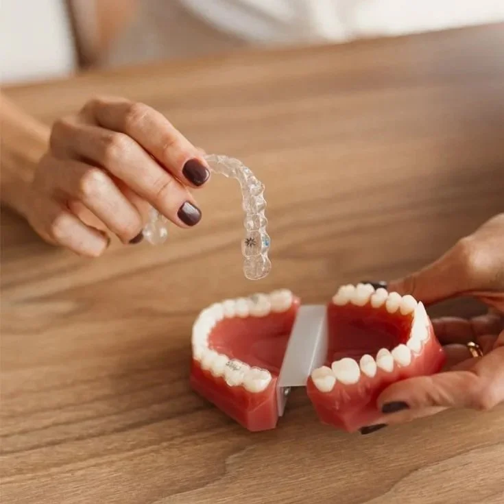 Pessoa segurando um aparelho ortodôntico transparente sobre um modelo de dentes em uma mesa de madeira.