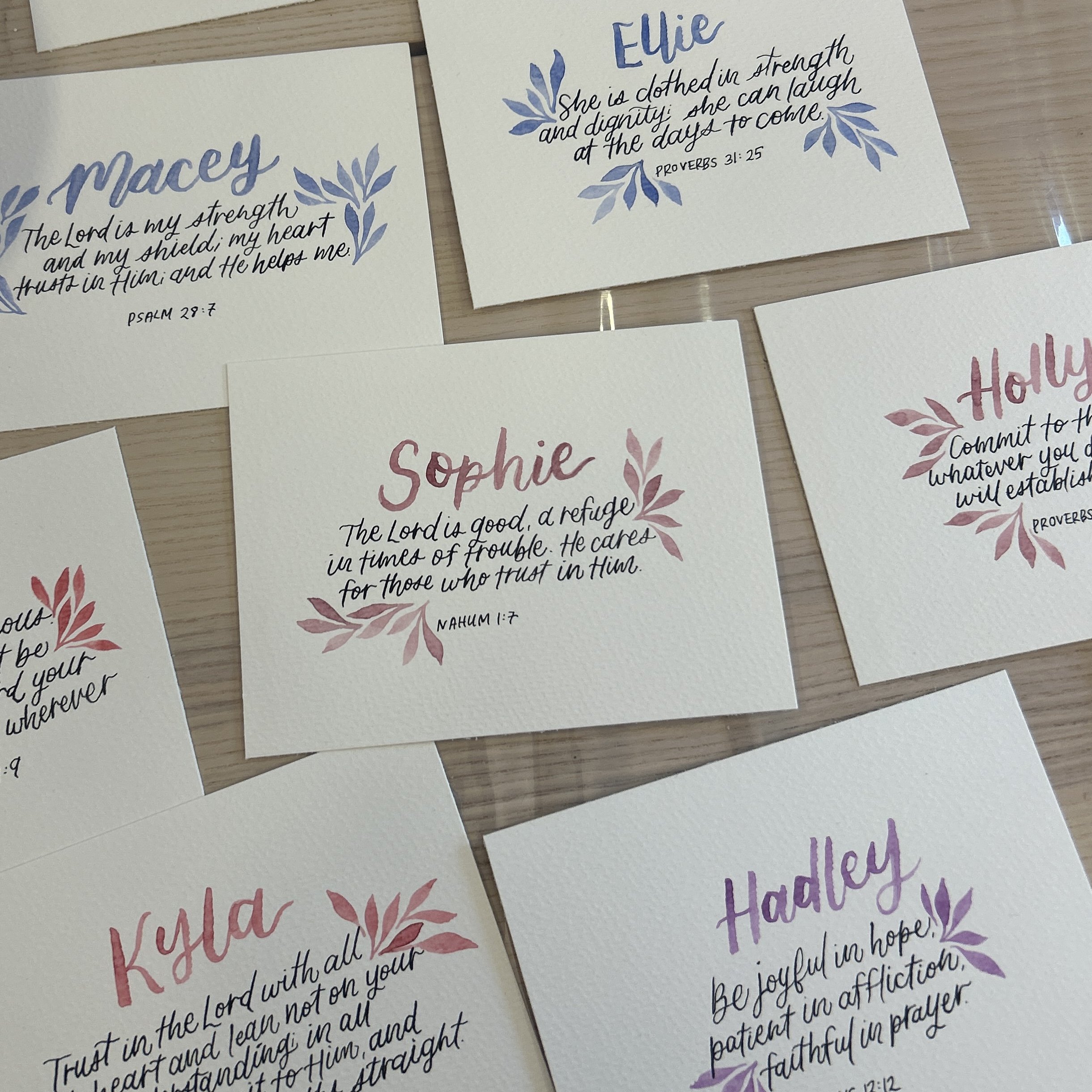 Handwritten inspirational Bible verses on decorative cards with floral accents, displayed on a wooden surface.