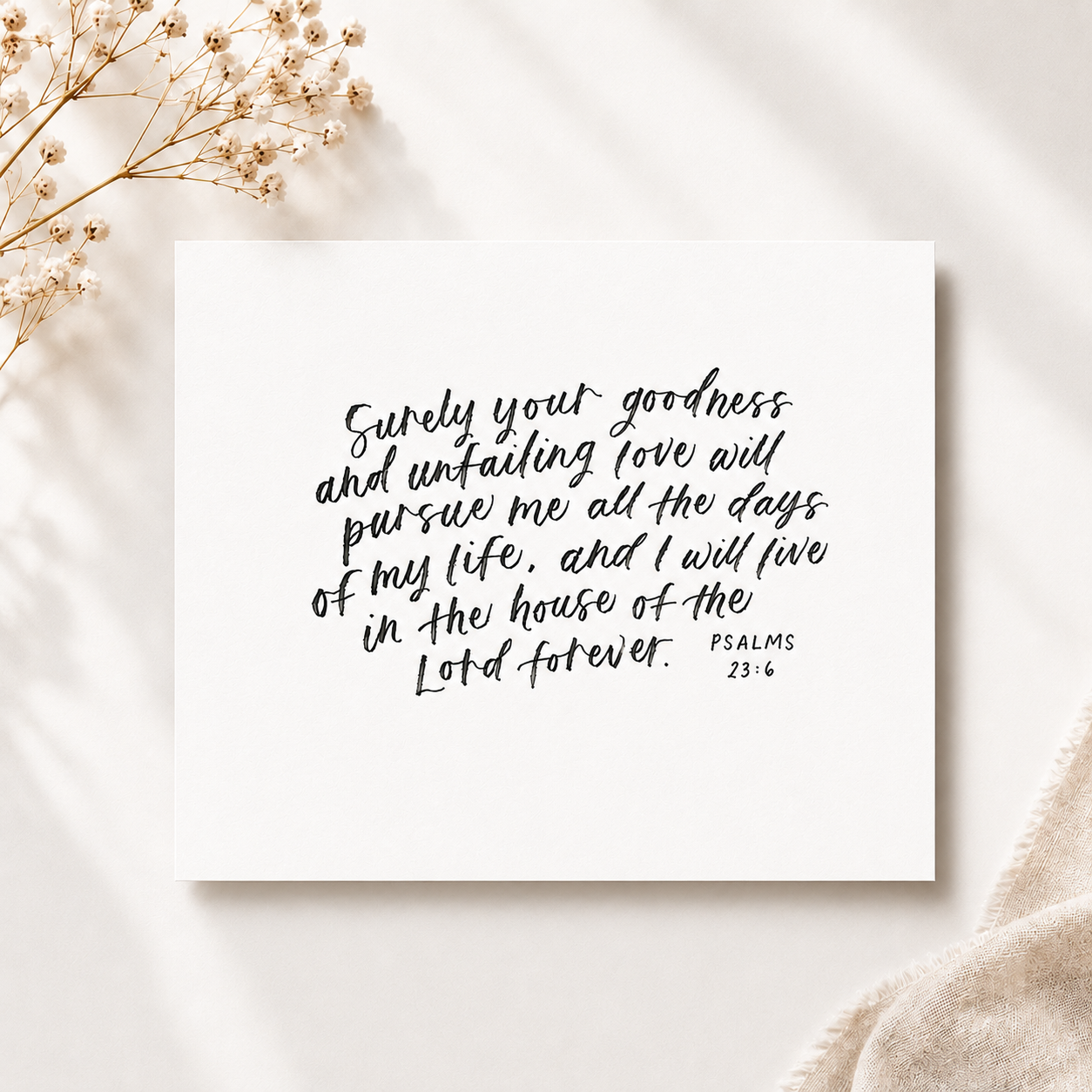 A handwritten quote on white paper that reads, "Surely your goodness and unfailing love will pursue me all the days of my life, and I will live in the house of the Lord forever. Psalms 23:6." The paper is placed on a light-colored surface, with a spr