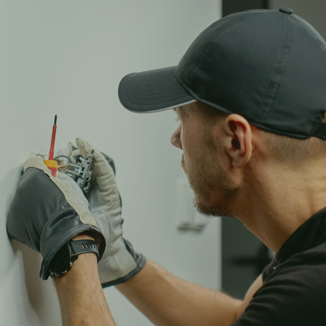 An electrician working on an electrical outlet with a screwdriver.