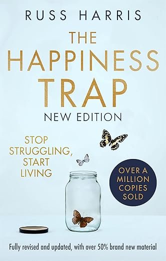 The book cover for 'The Happiness Trap' by Russ Harris features a light blue background with text and images. The title is in large gold letters, with the author's name at the top. A glass jar at the bottom has three butterflies flying out, symbolizing freedom or happiness. Additional text includes 'Stop struggling, start living' and mentions that over a million copies have been sold. The cover indicates it is the 'New Edition' and is fully revised with over 50% new material.