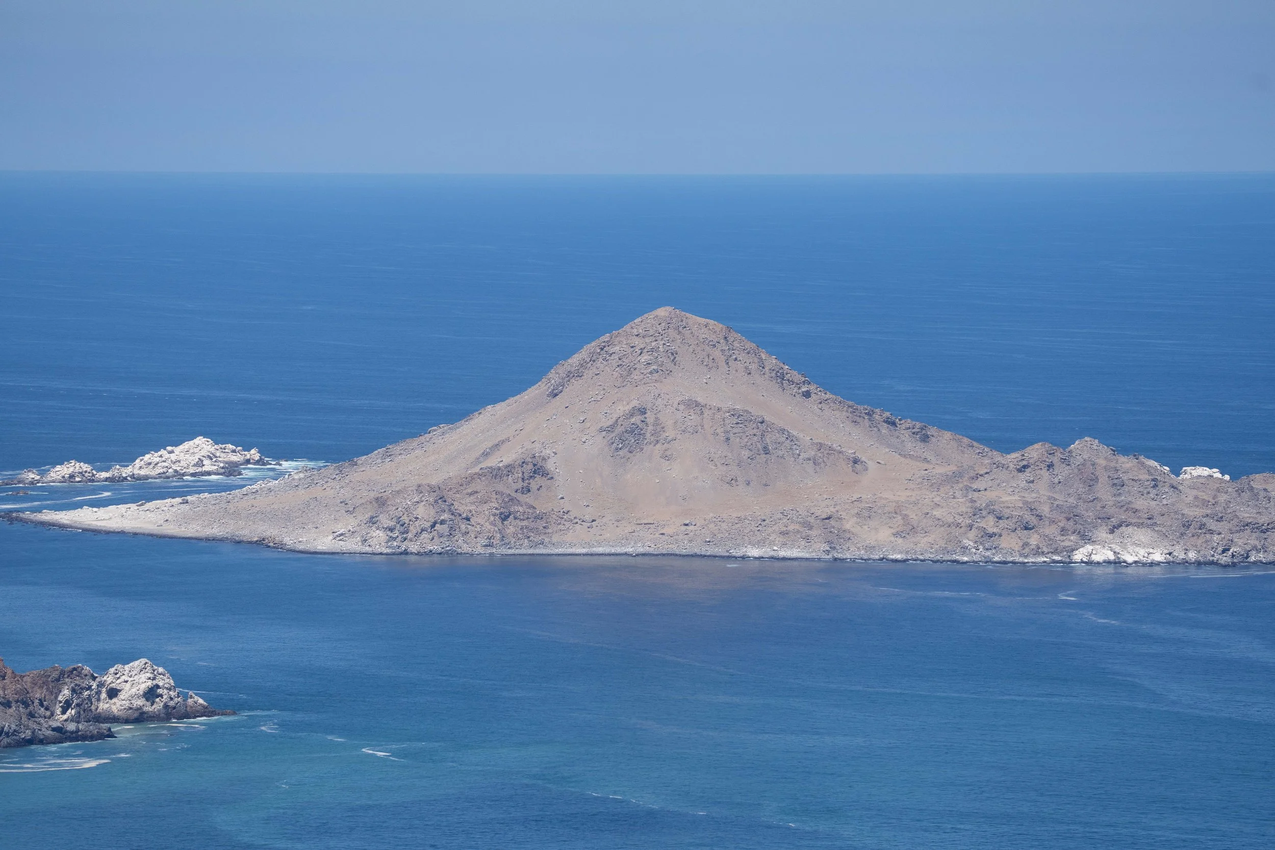 Une île rocheuse au centre de l'océan, avec une montagne ou un volcans sableux, entourée d'eau bleue.