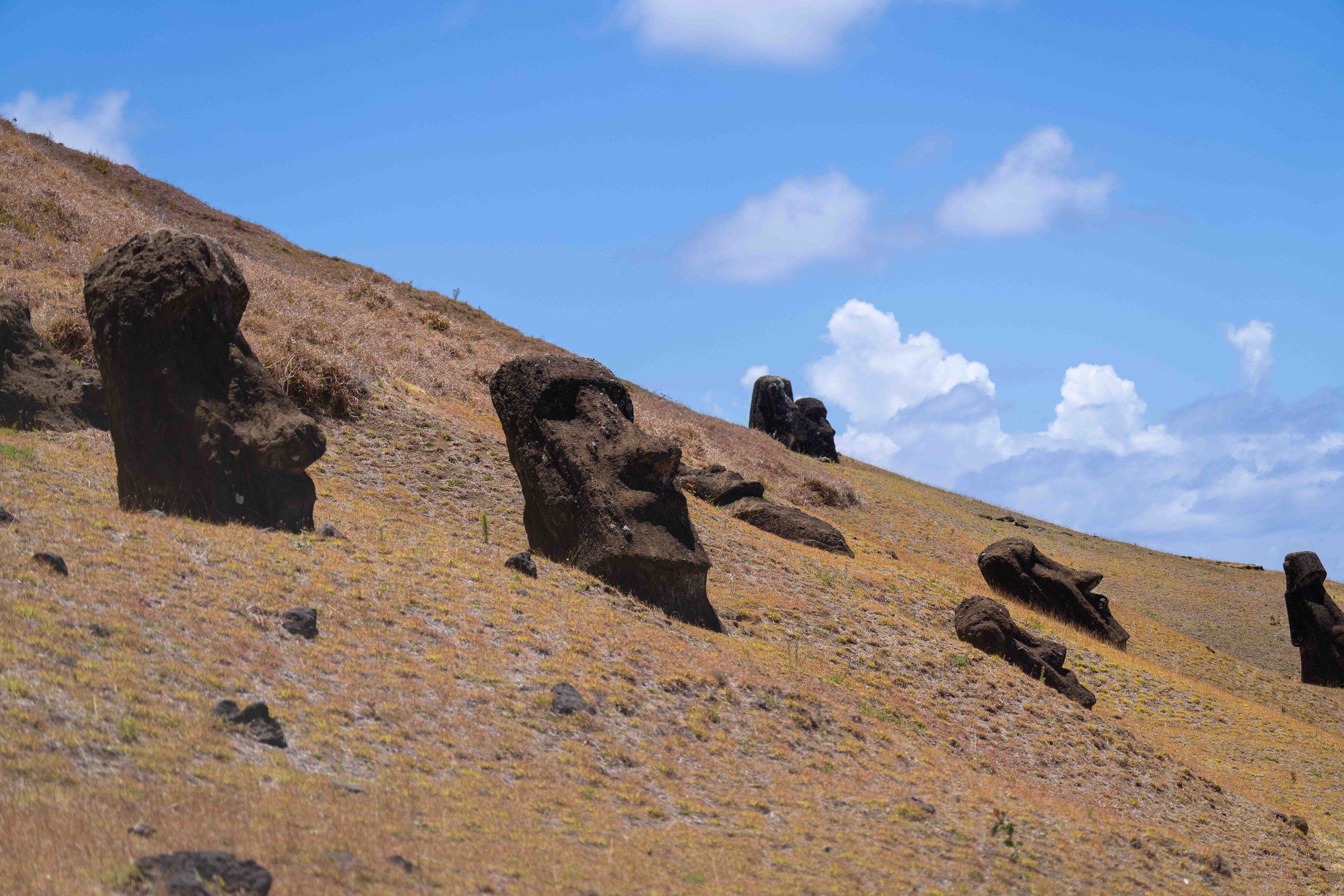 Les statues Moai sur une colline de l'île de Pâques, sous un ciel bleu avec quelques nuages.