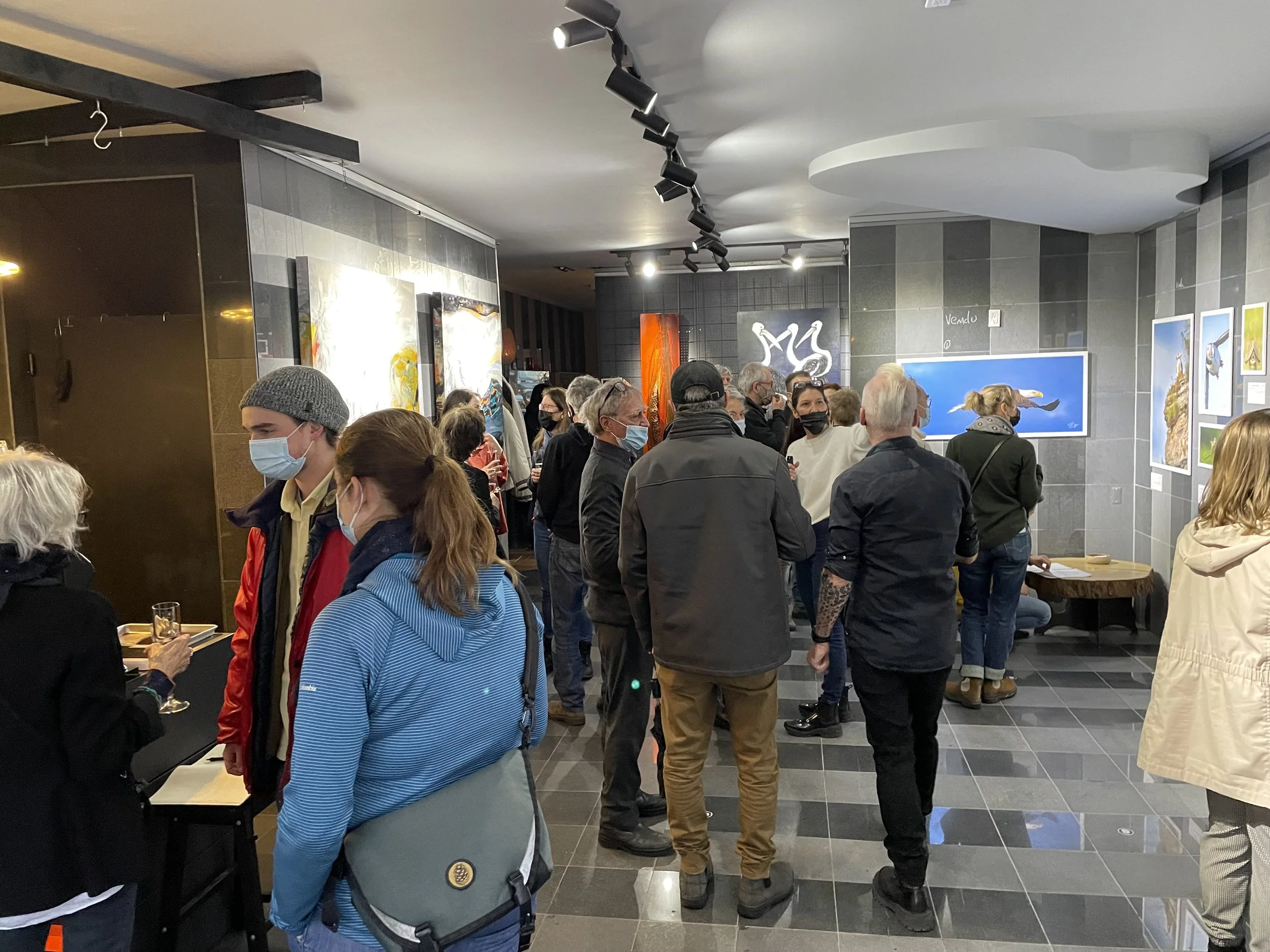 Gens dans une galerie d'art, observant diverses œuvres exposées au mur dans un espace intérieur moderne et bien éclairé.