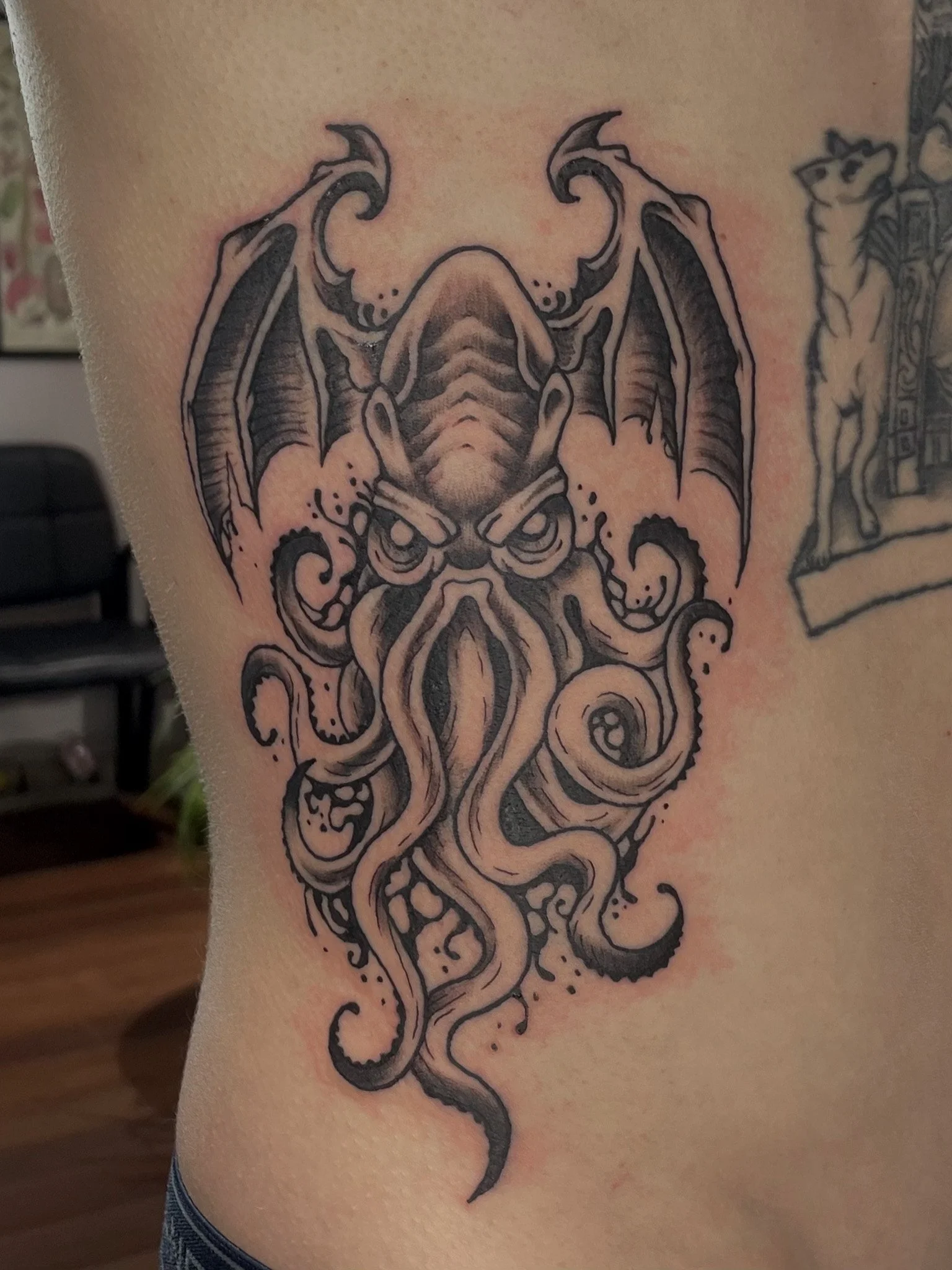 Tattoo of a menacing octopus with a dragon-like head and wings on a person's side.