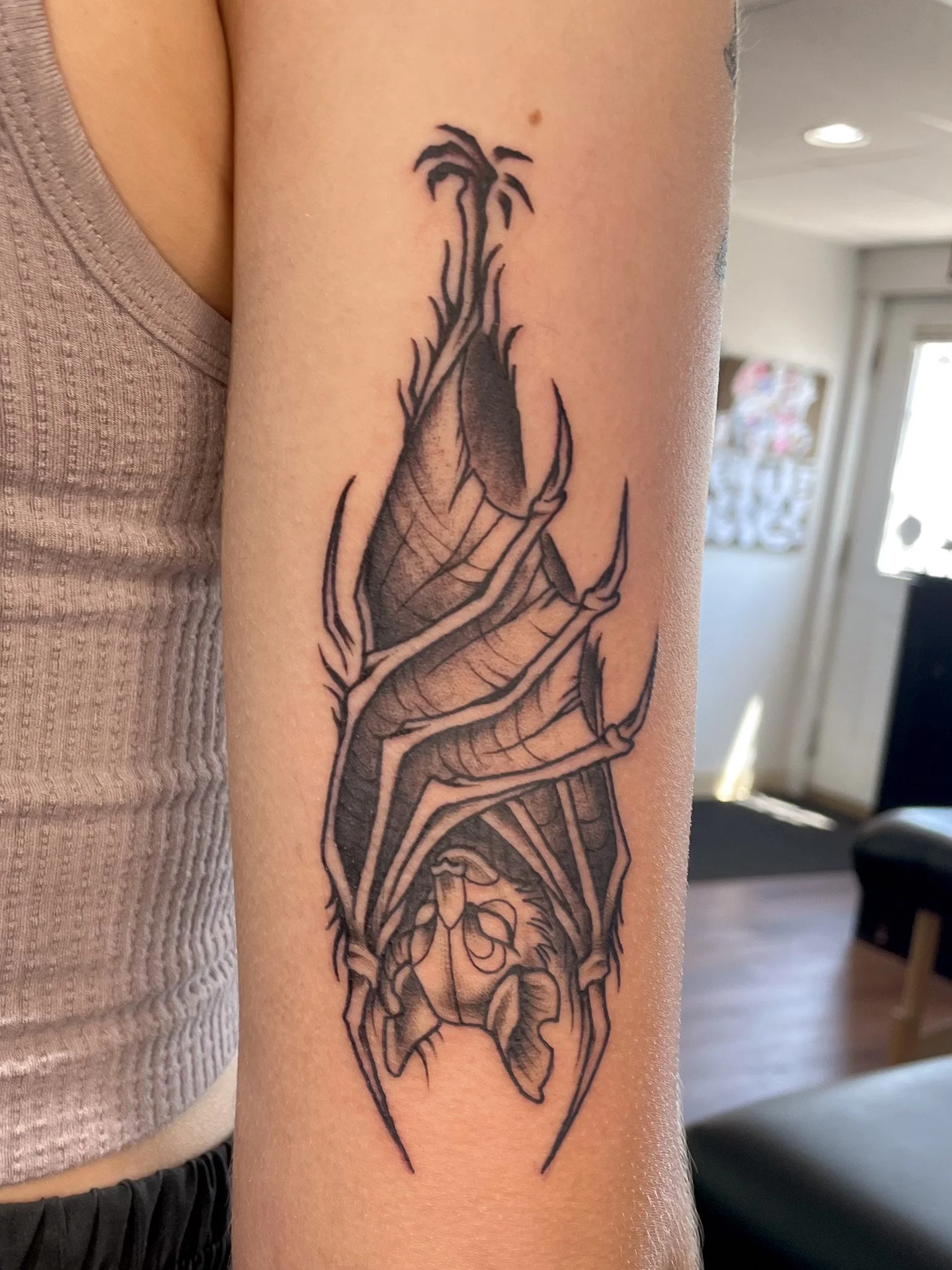 Black and gray tattoo of a spider hanging upside down with its legs curled underneath, detailed web pattern, on a person's upper arm.