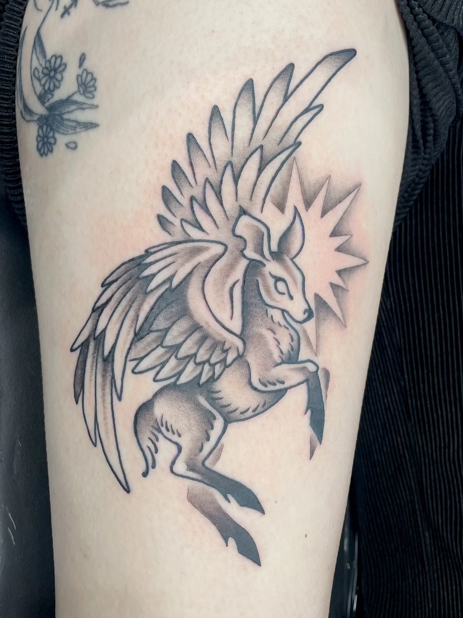 Tattoo of a mythical creature with the body of a lion and the head and wings of a bird, with a radiating star behind its head.